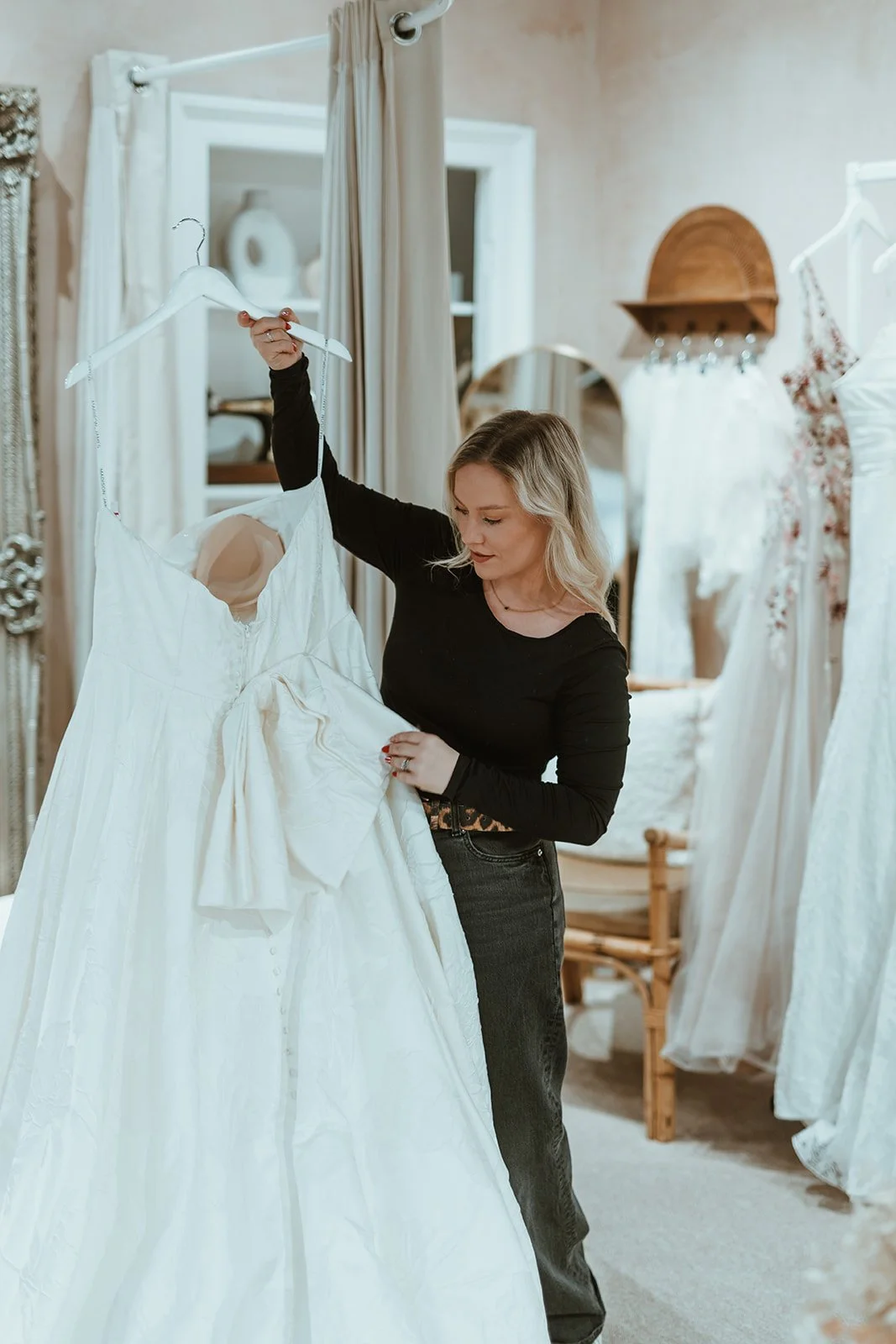 A woman in black clothes shopping for dresses in a boutique, holding a white wedding dress on a hanger.
