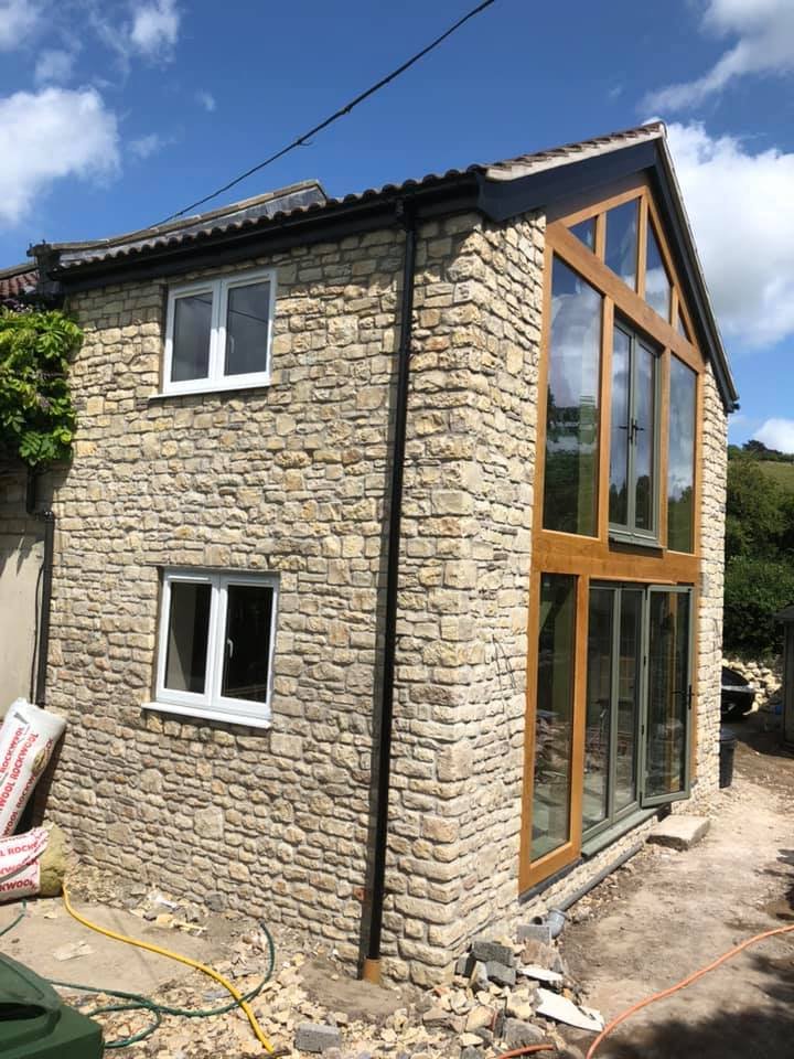 A two-story house with stone exterior walls and large glass windows with wooden frames, including a gabled roof.