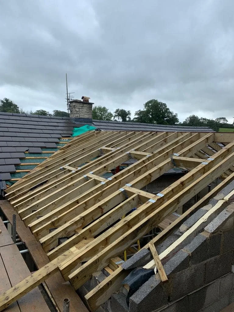 Construction of a new roof with wooden framing over an existing house, with roofing tiles partially installed.