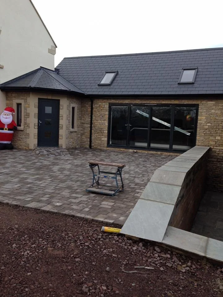 Newly constructed brick and stone house with patio, sliding glass door, and skylights on the roof, decorated with a Santa Claus inflatable, and construction tools and materials present.