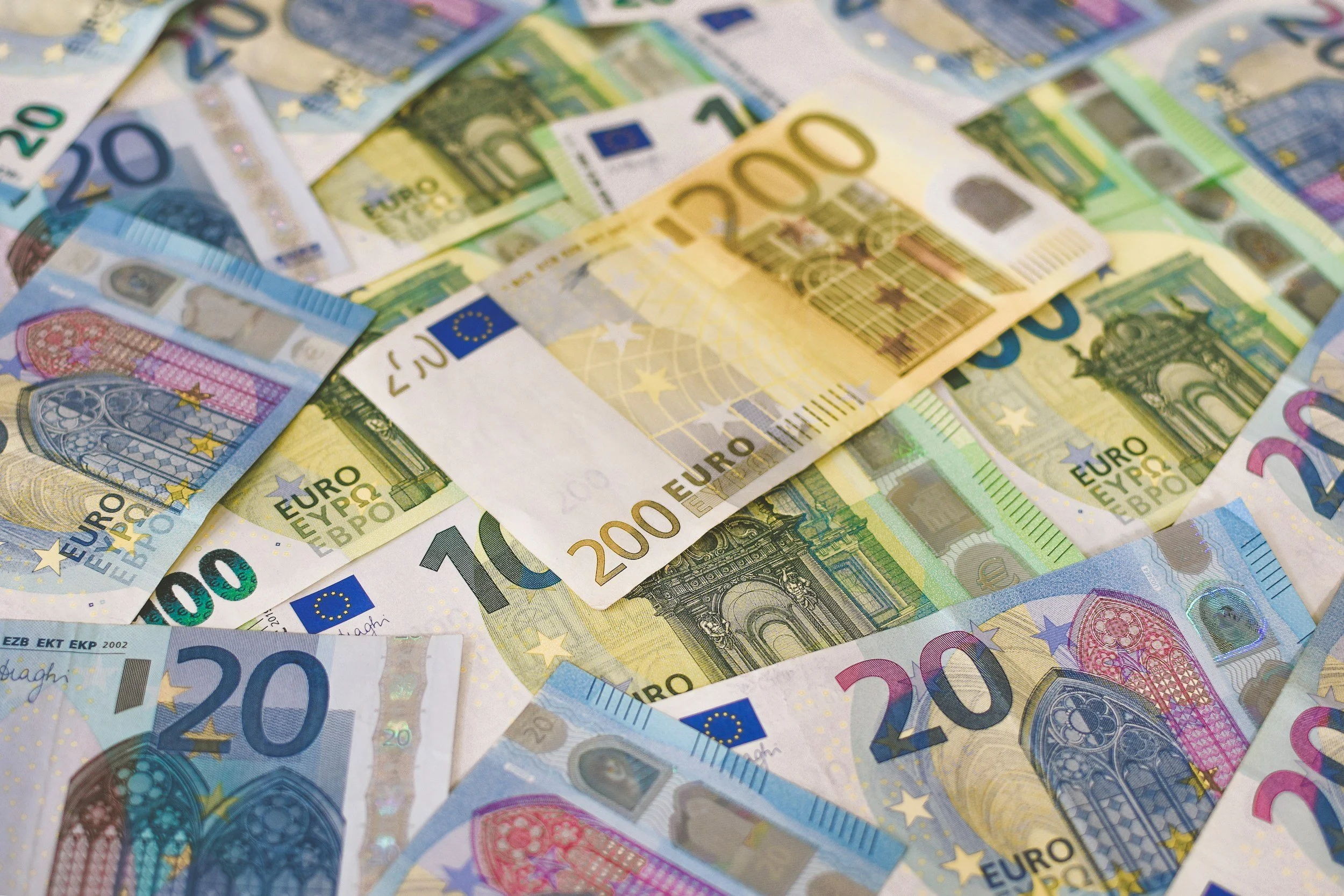 A collection of euro banknotes in various denominations, including 20, 100, and 200 euros, spread out and overlapping.