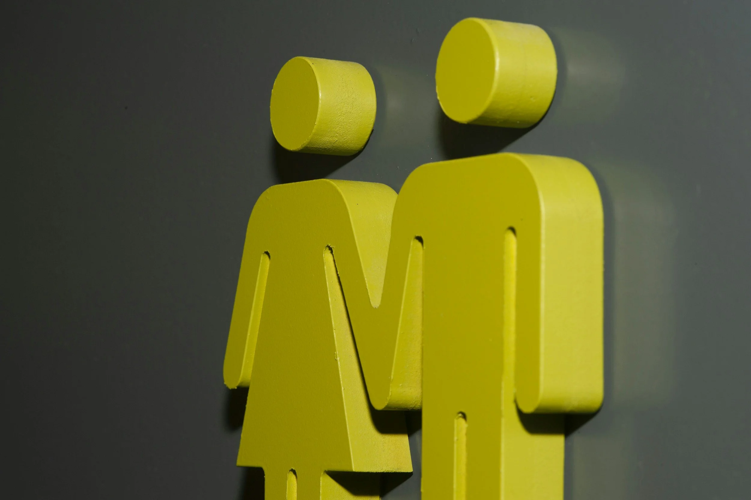 Yellow 3D male and female restroom signs attached to a dark wall.