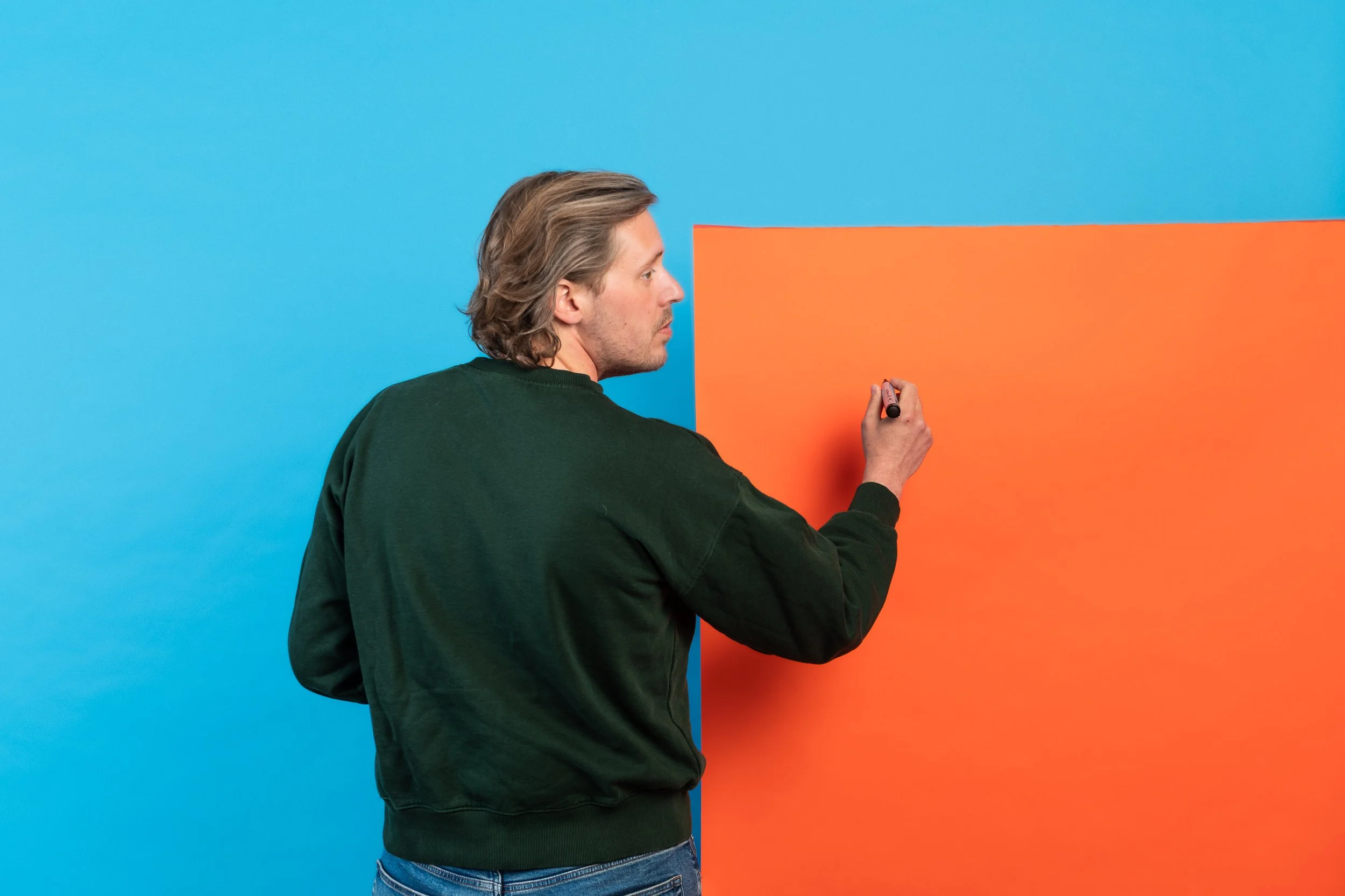 Man schrijft op een geel/oranje bord dat tegen een blauw/oranje achtergrond staat.