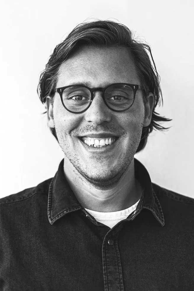 Lachende man met brillen en denim jas, zwart-wit foto.