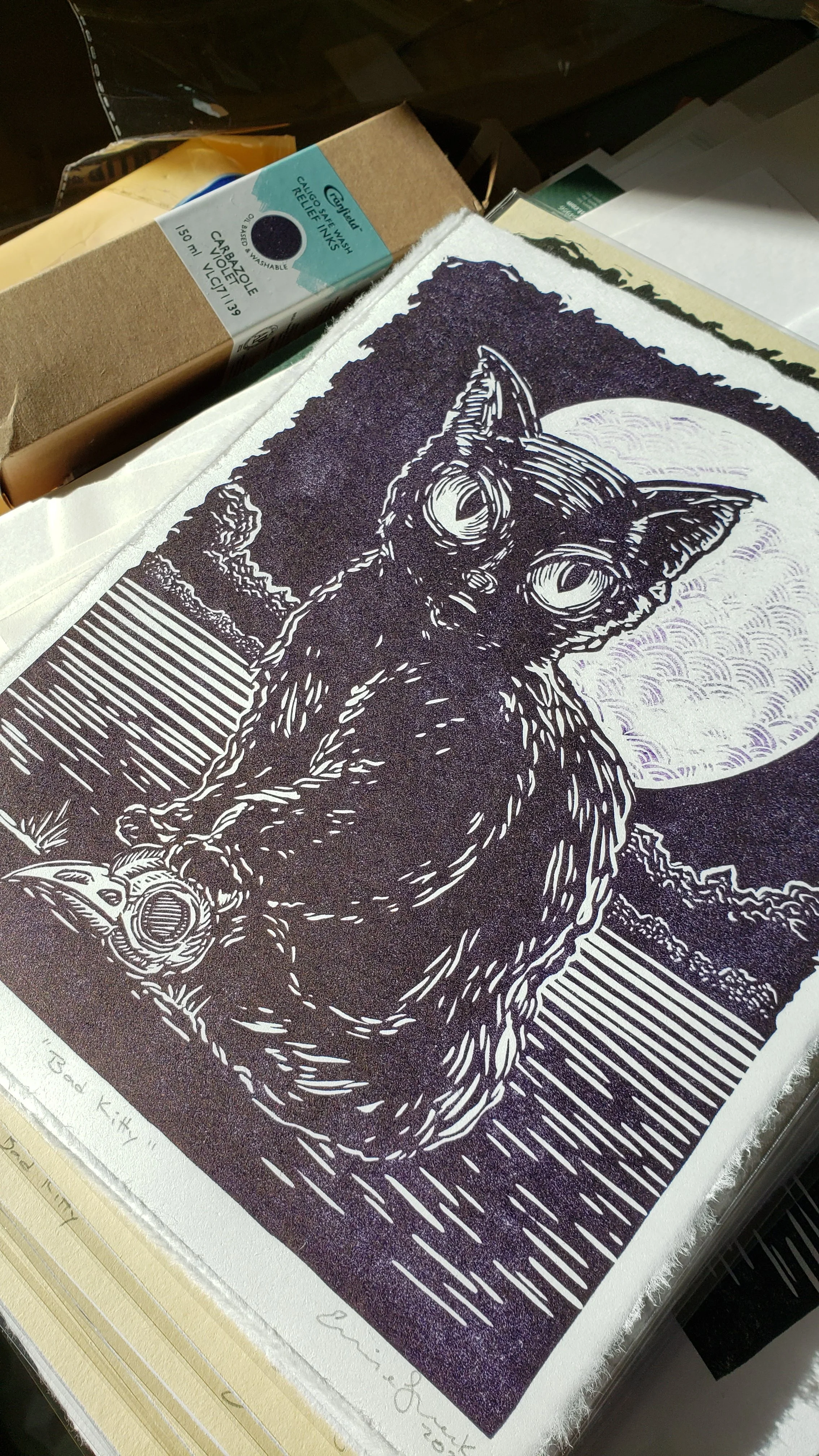 stack of signed prints next to box of ink color used in printing