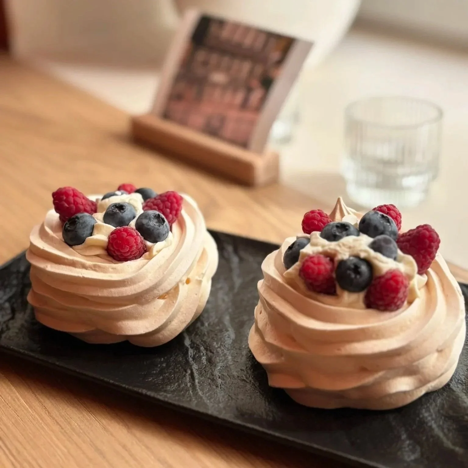 Two decorative meringue desserts topped with mixed berries, served on a black plate.