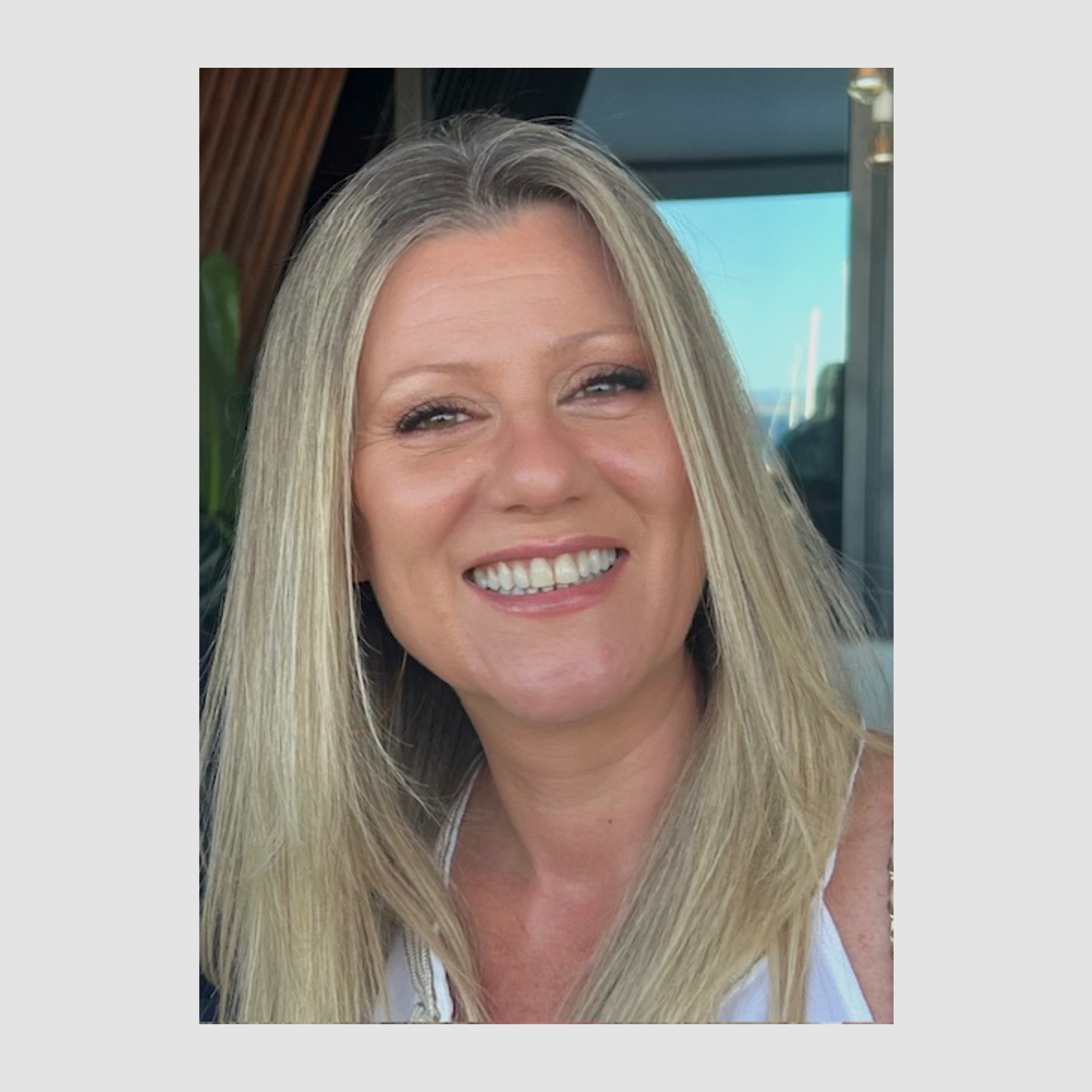 Mulher sorridente com cabelo loiro longo, usando maquiagem suave, no ambiente de um restaurante ou café