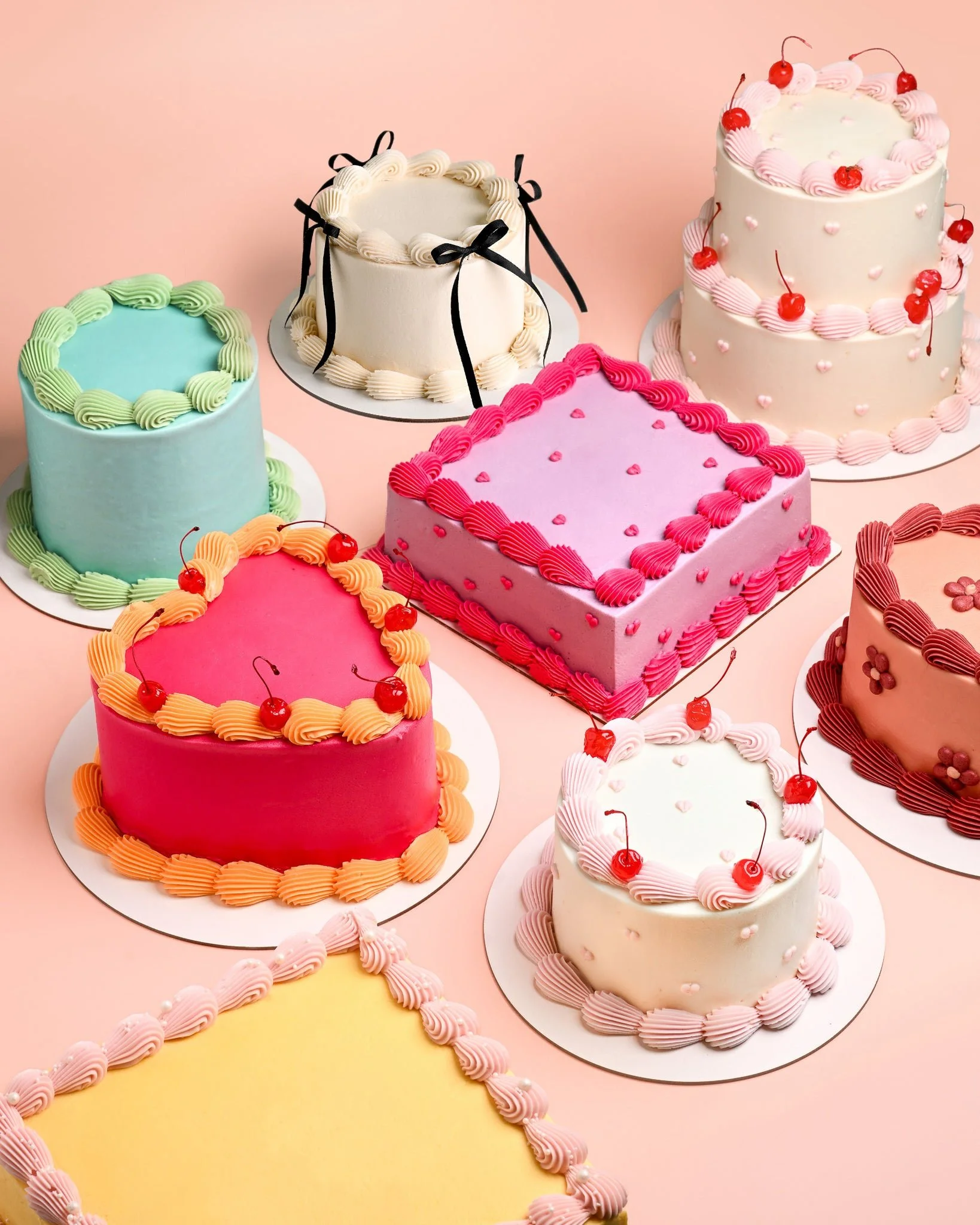 Various decorated cakes with colorful frosting, cherries, and decorative elements on a pastel background.