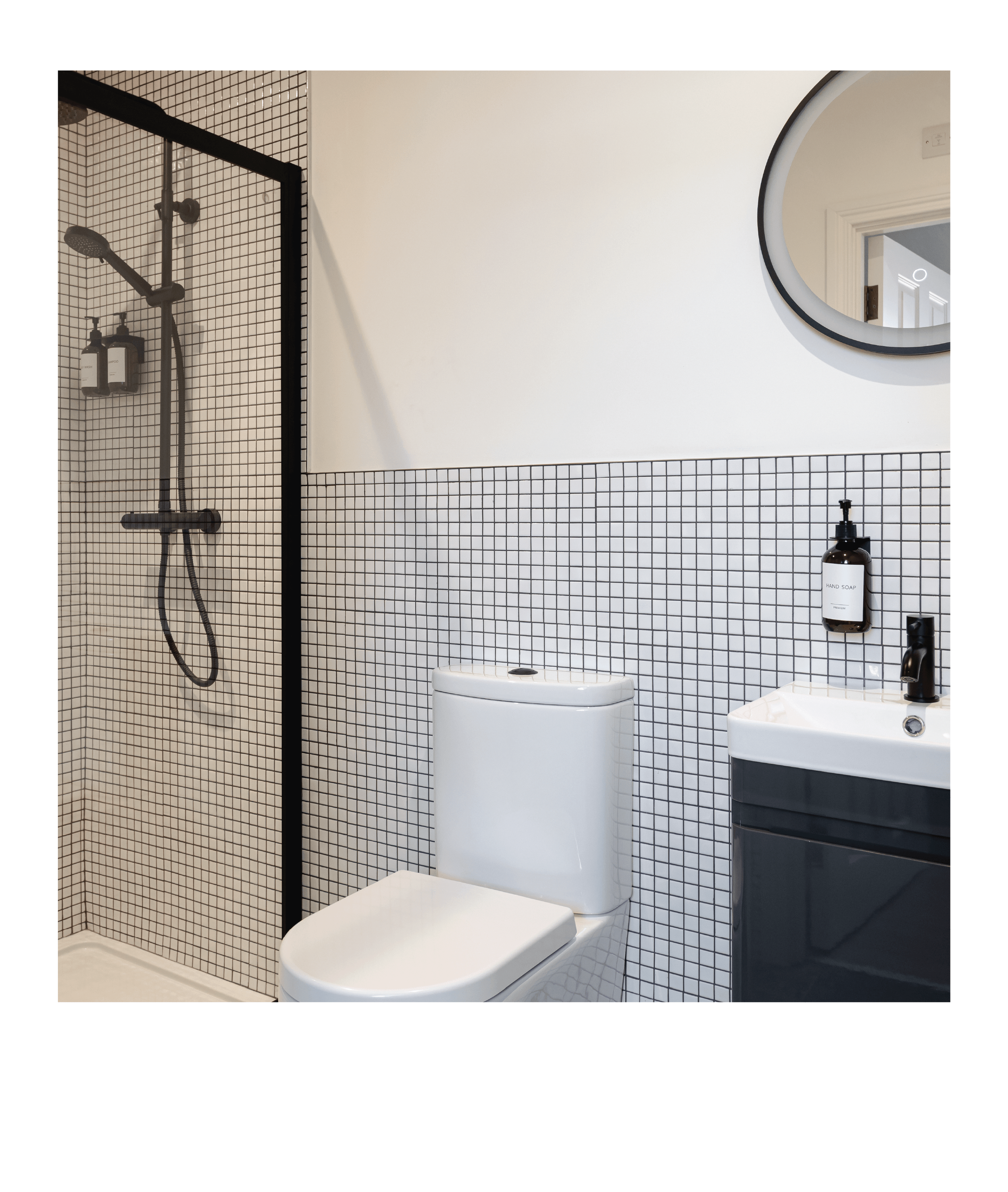 Modern bathroom with white and black color scheme, featuring a walk-in shower with black frame and black grid tiles, a white toilet, a small white sink with black fixtures, a hand soap dispenser on the wall, a round mirror with black frame, and a minimalistic design.