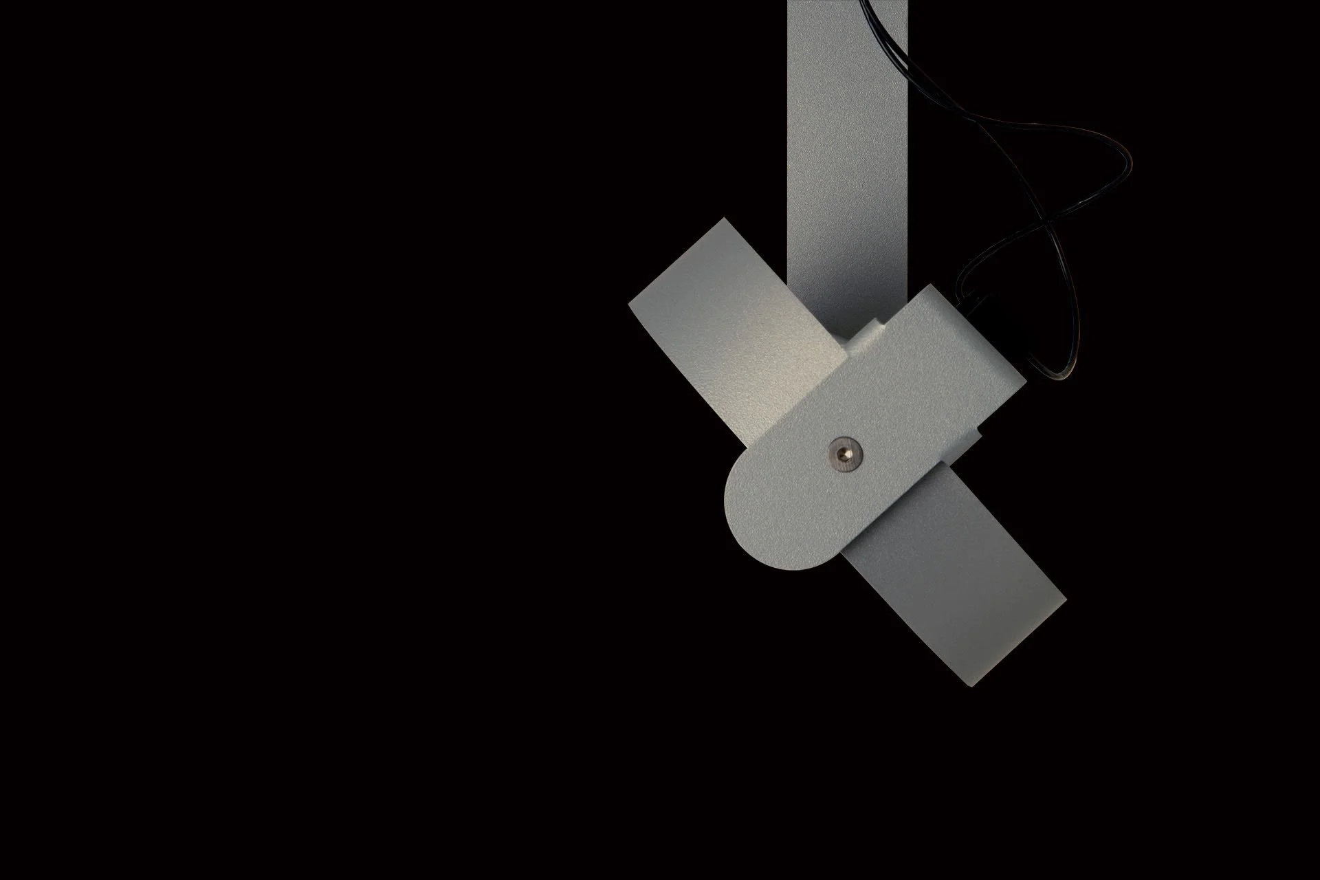 A close-up of a metallic, industrial-looking machine part with a screw and a black cord, against a black background.