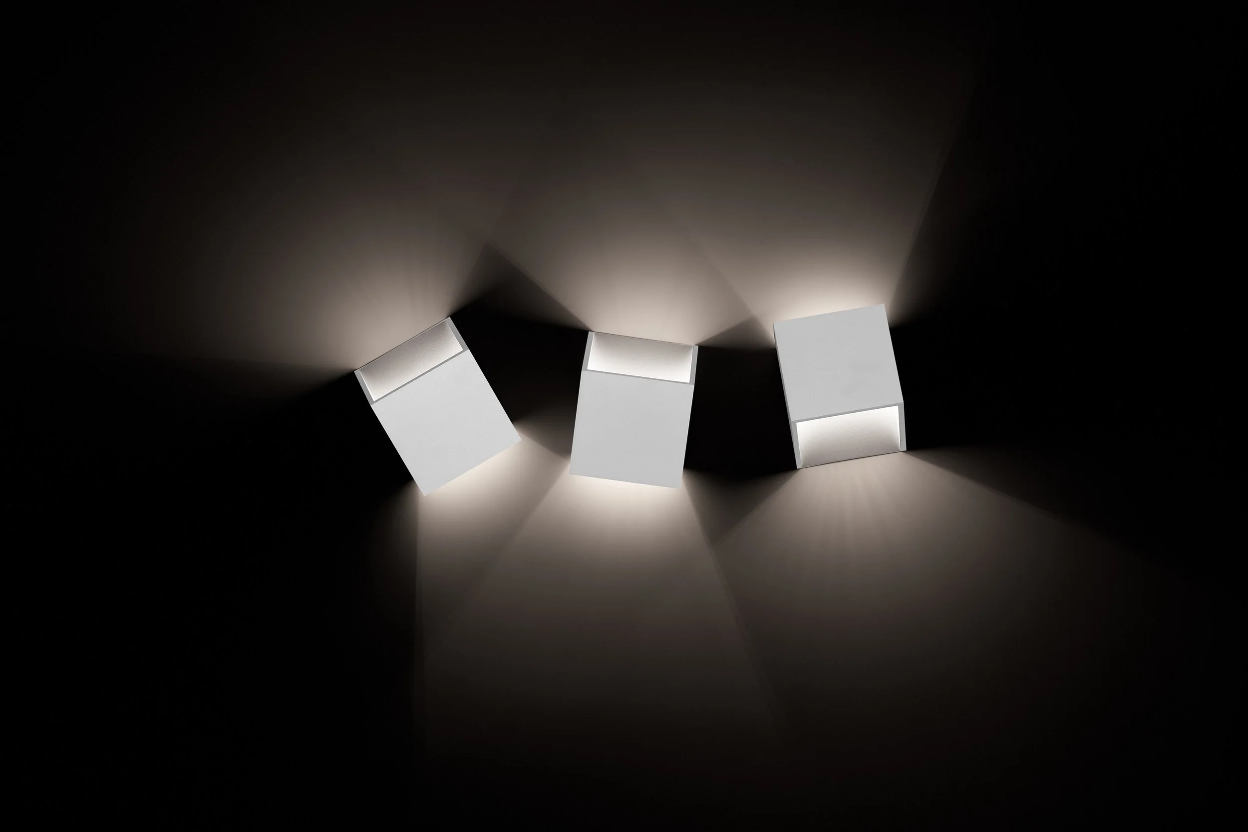 Three white cube-shaped objects on a dark surface, casting light and shadows outward.