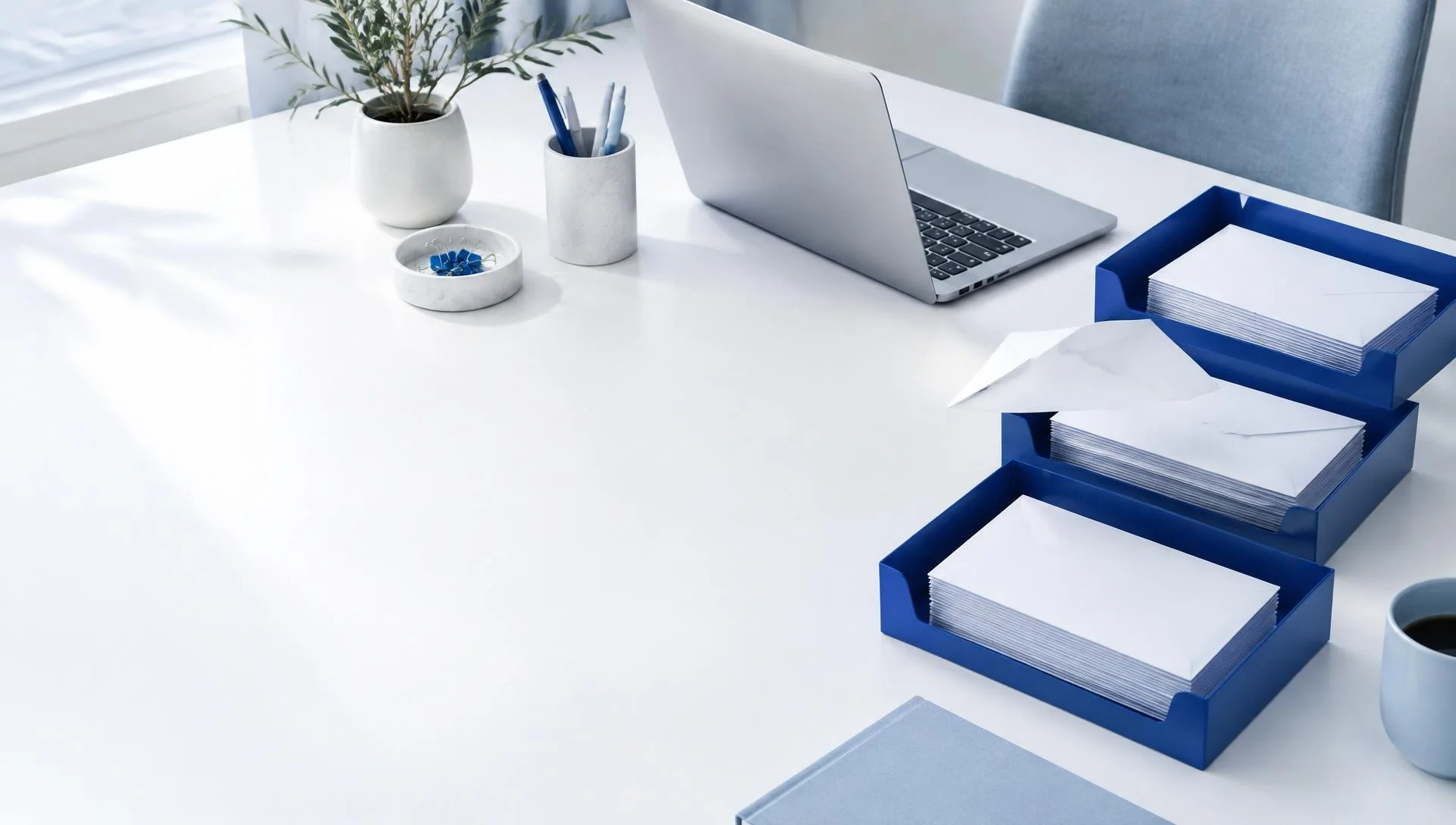 A calm, orderly stack of envelopes sorted into neat blue trays on a bright desk