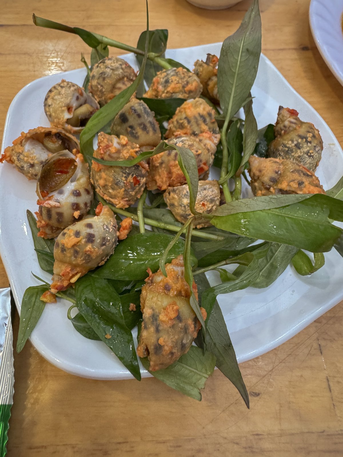 Grilled sea snails with herbs and chili on a plate, one of several snail preparations sampled in Ho Chi Minh City.