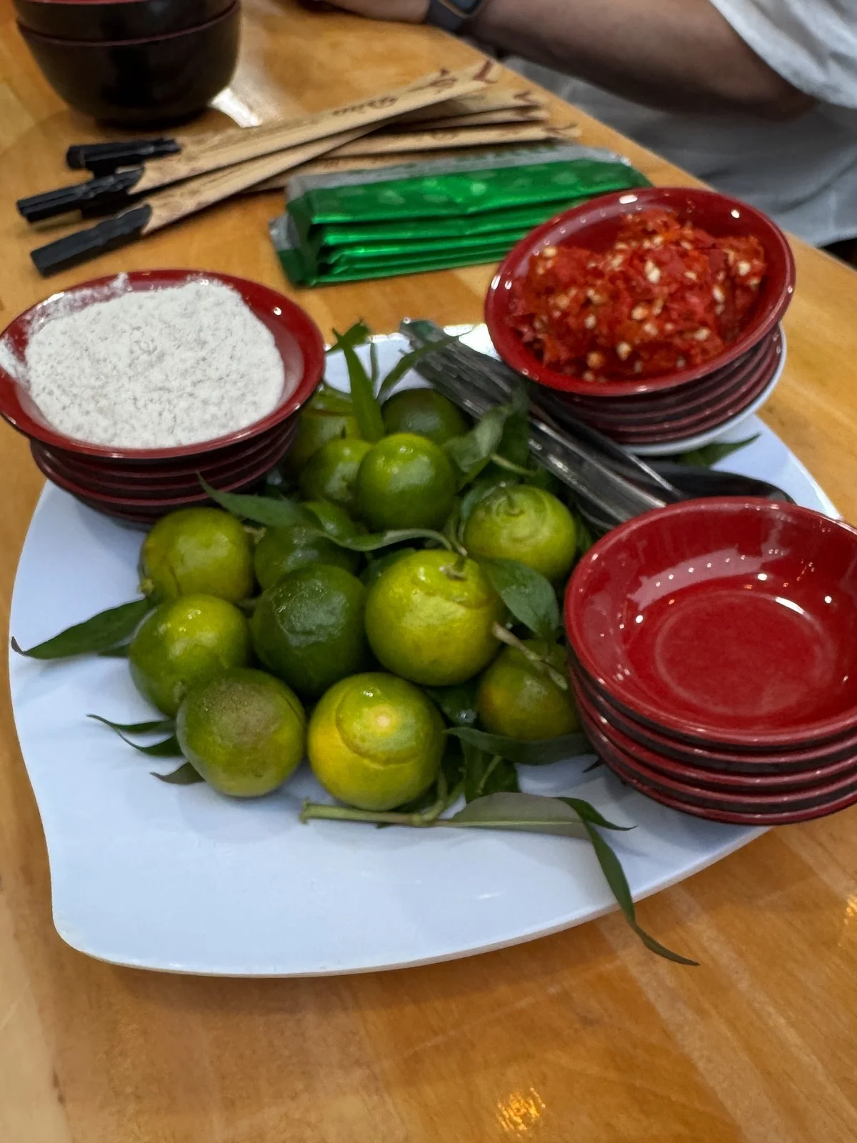 A plate of kumquats, chili salt, and dipping sauces served alongside a Vietnamese street food dish in Ho Chi Minh City.