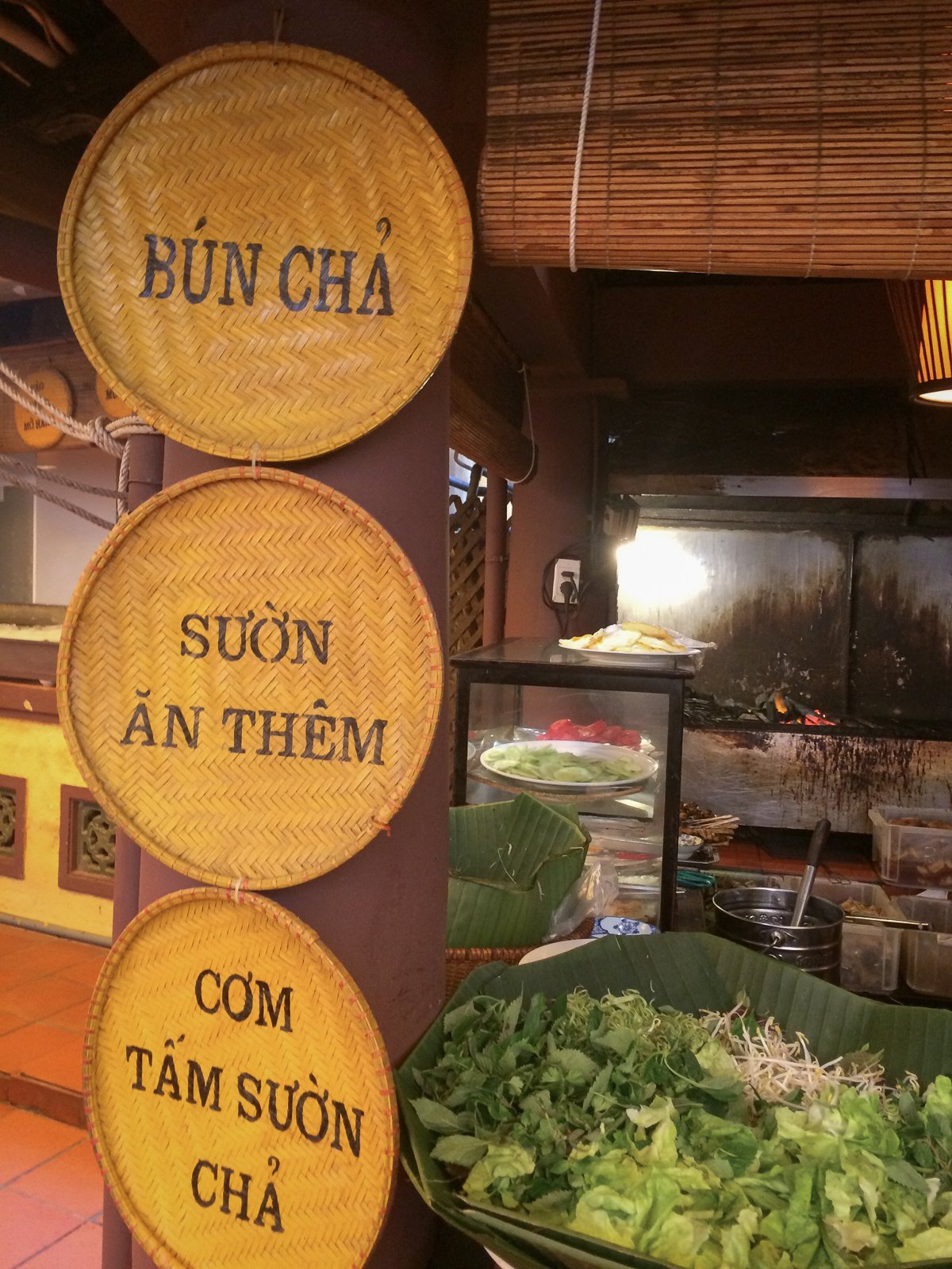 Woven signs advertise bún chả and rice plates at a Vietnamese street food stall. 