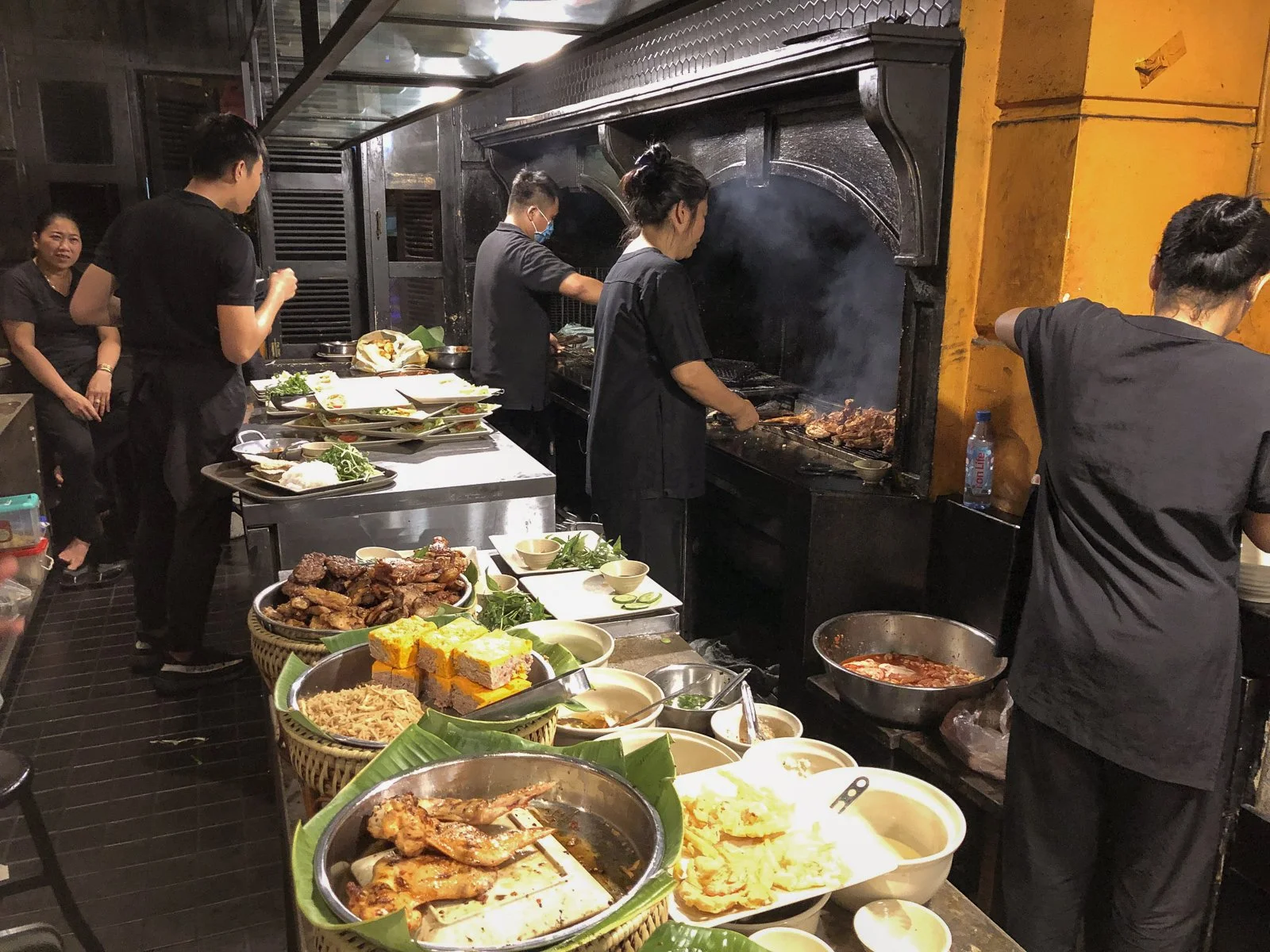 Cooks grill meats and plate dishes at a multi-vendor Ho Chi Minh City food hall. 
