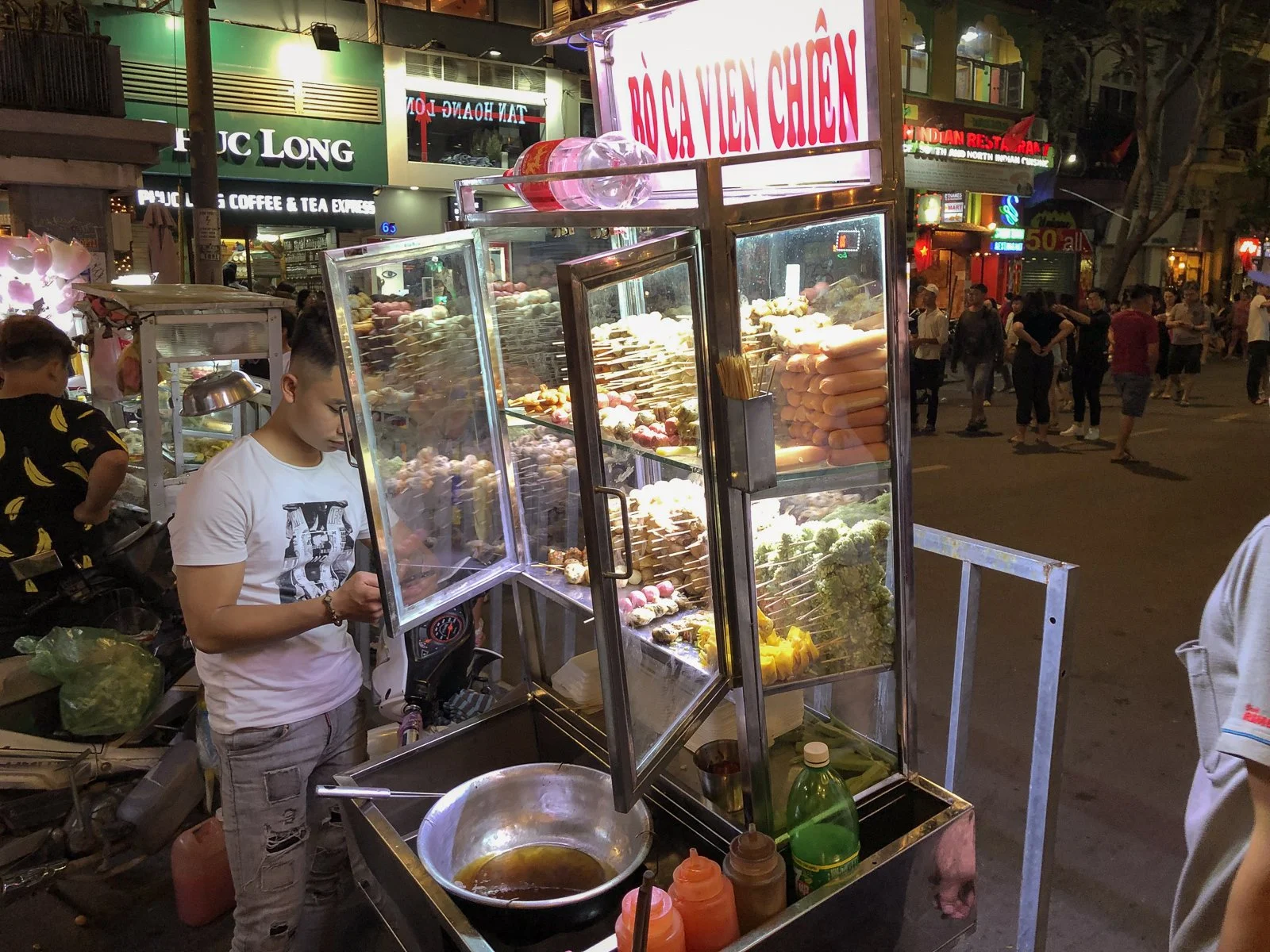 A Ho Chi Minh City street cart sells grilled meatball and sausage skewers at night. 