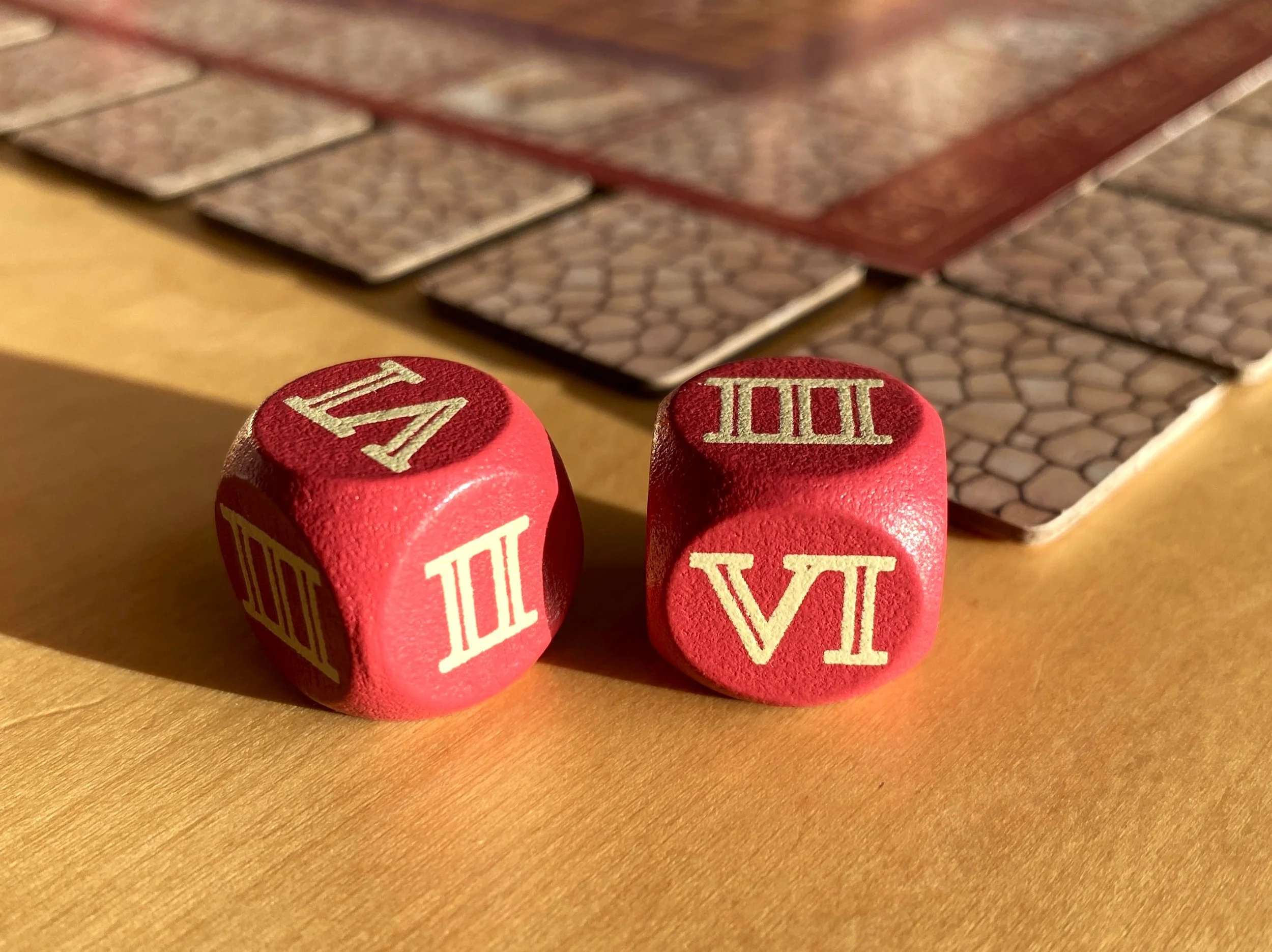 Red wooden dice with Roman numerals from the Escape From Pompeii board game