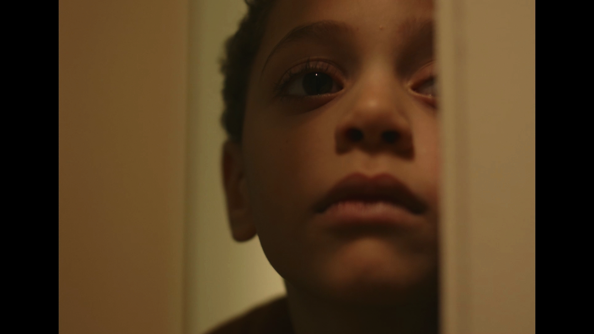 Close-up of a young child's face peeking from behind a door, with a curious or contemplative expression.