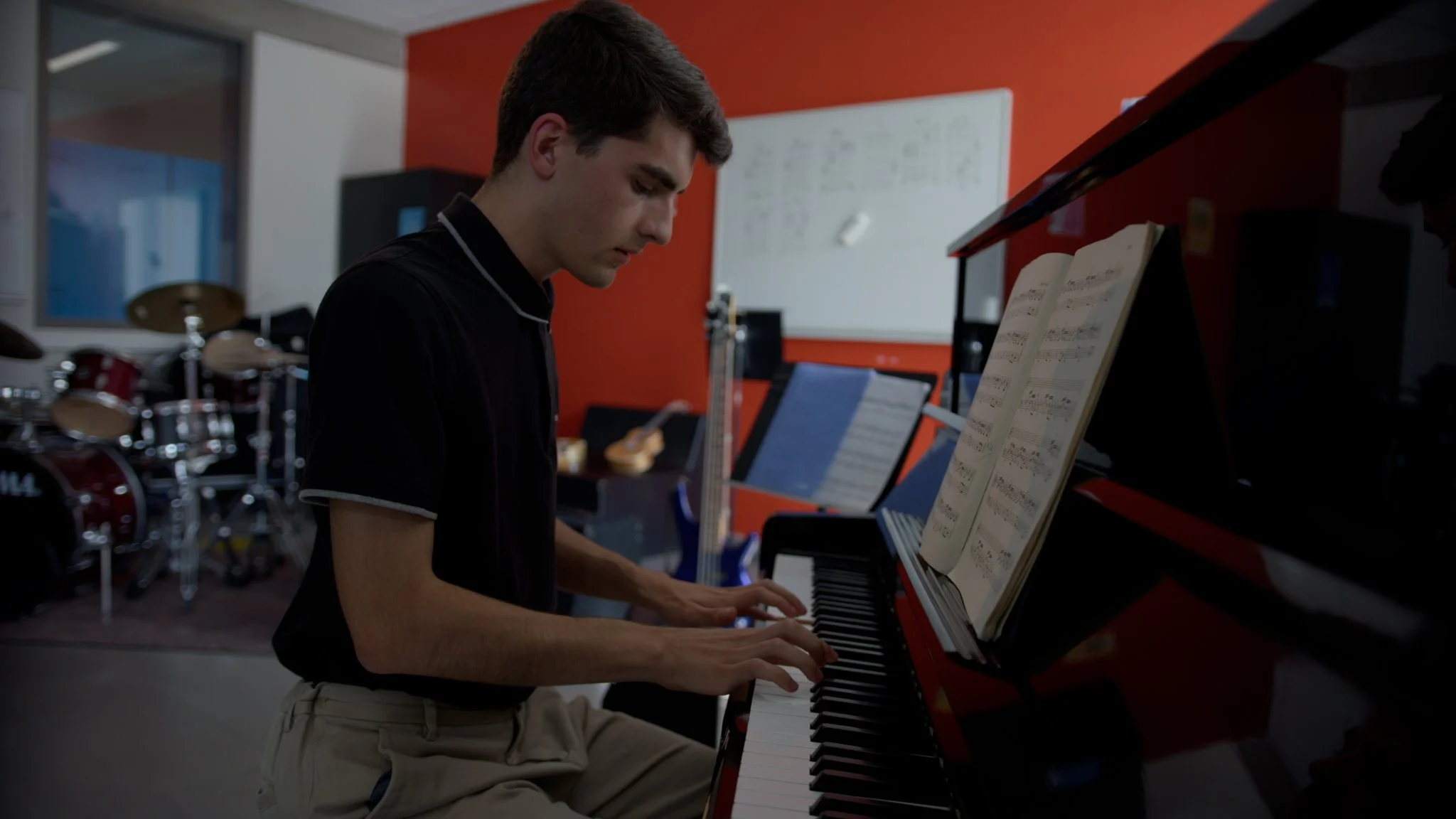 Young man playing the piano with sheet music in a music studio.
