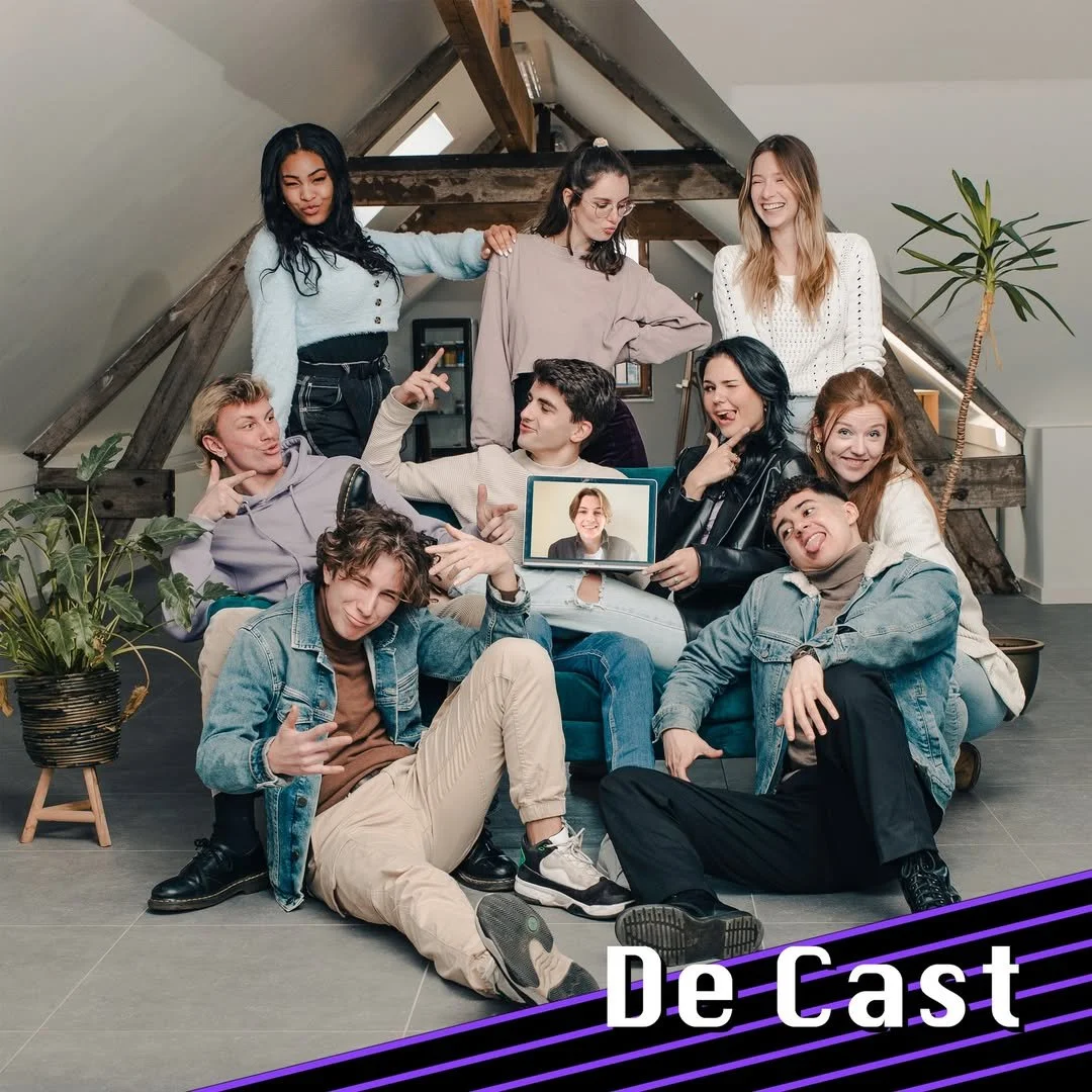 Group of ten young adults gathering in a bright, attic-style room, with some sitting on a sofa and others standing behind, engaging in a virtual video call with a woman displayed on a laptop. They are smiling, laughing, and making playful gestures, surrounded by indoor plants and wooden beams.