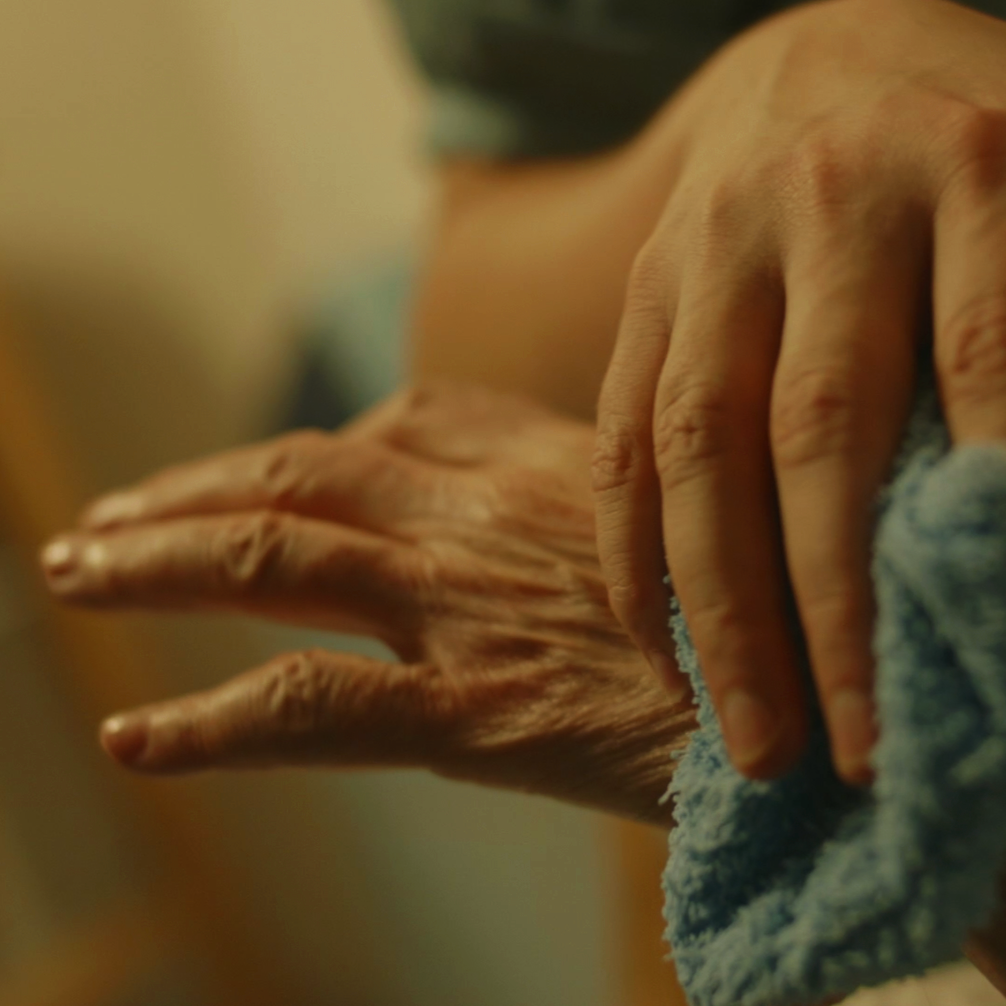 Close-up of an elderly person's hand with visible wrinkles, holding a soft blue cloth.