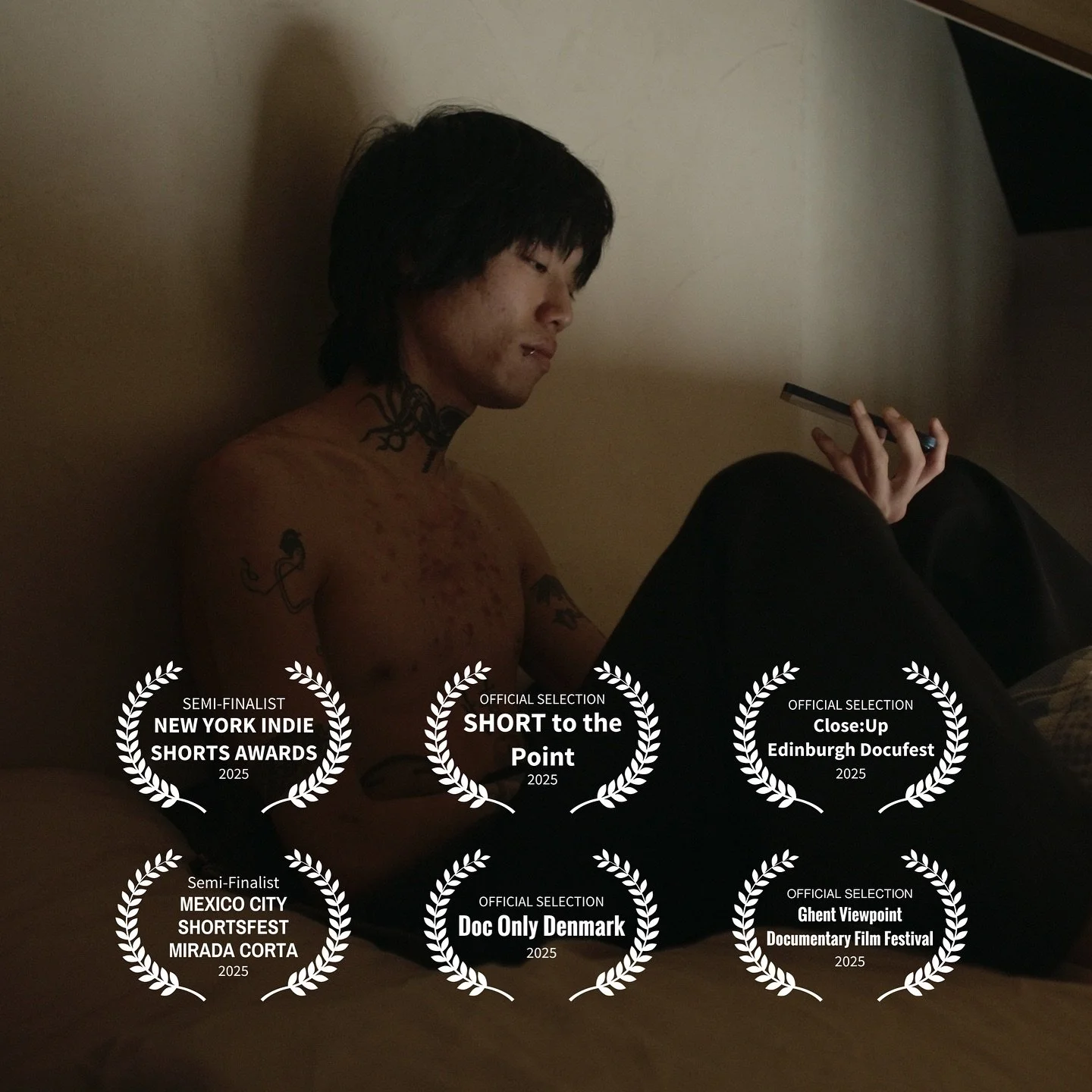 A shirtless man with tattoos, sitting against a wall, looking at his phone in a dimly lit room, with award laurels overlayed indicating film festival nominations and selections.