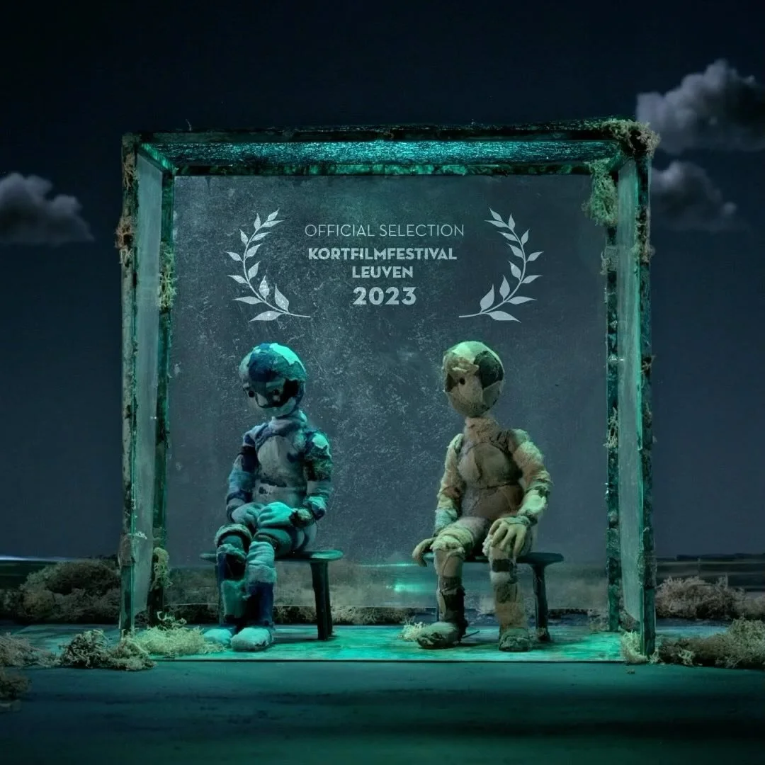 Two astronauts seated on benches under a neon-lit frame at night, with a sign reading 'Official Selection Kortfilmfestival Leuven 2023', in a surreal, space-themed setting.