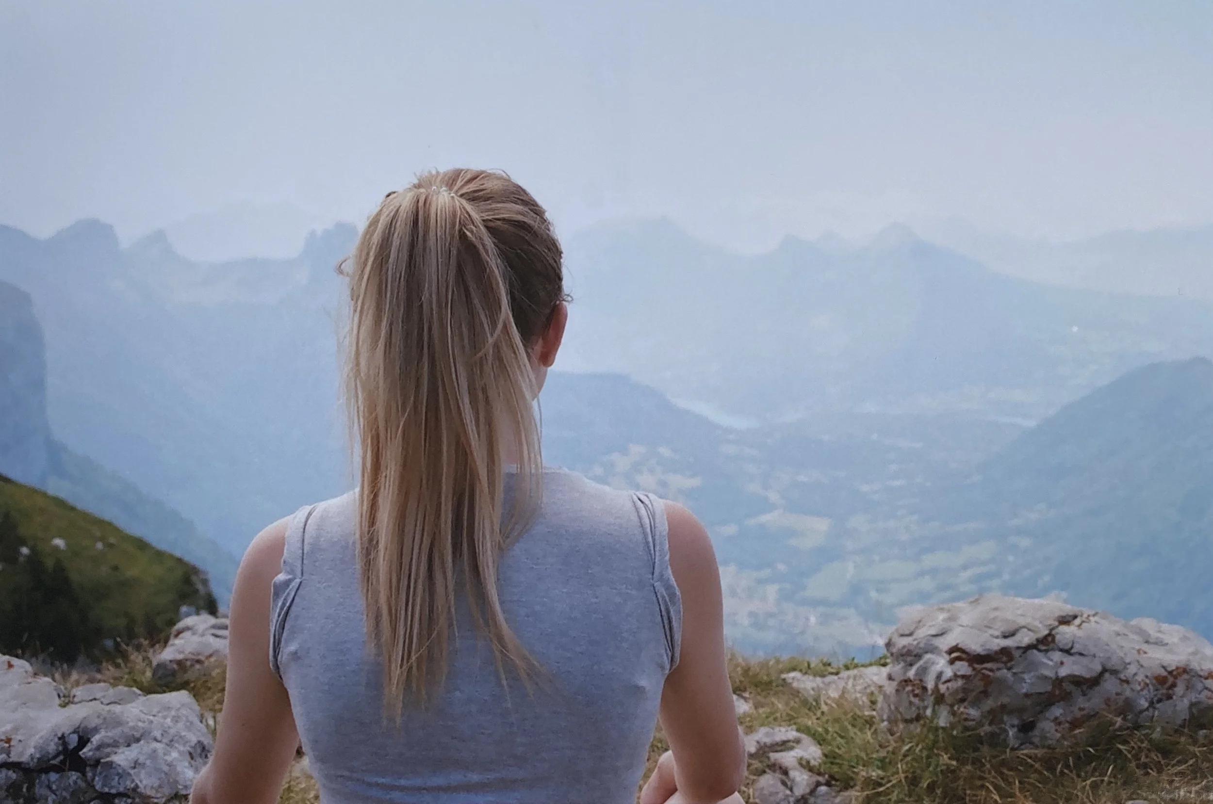 Femme vue de dos, regardant un paysage de montagnes et vallée, en posture de méditation.
