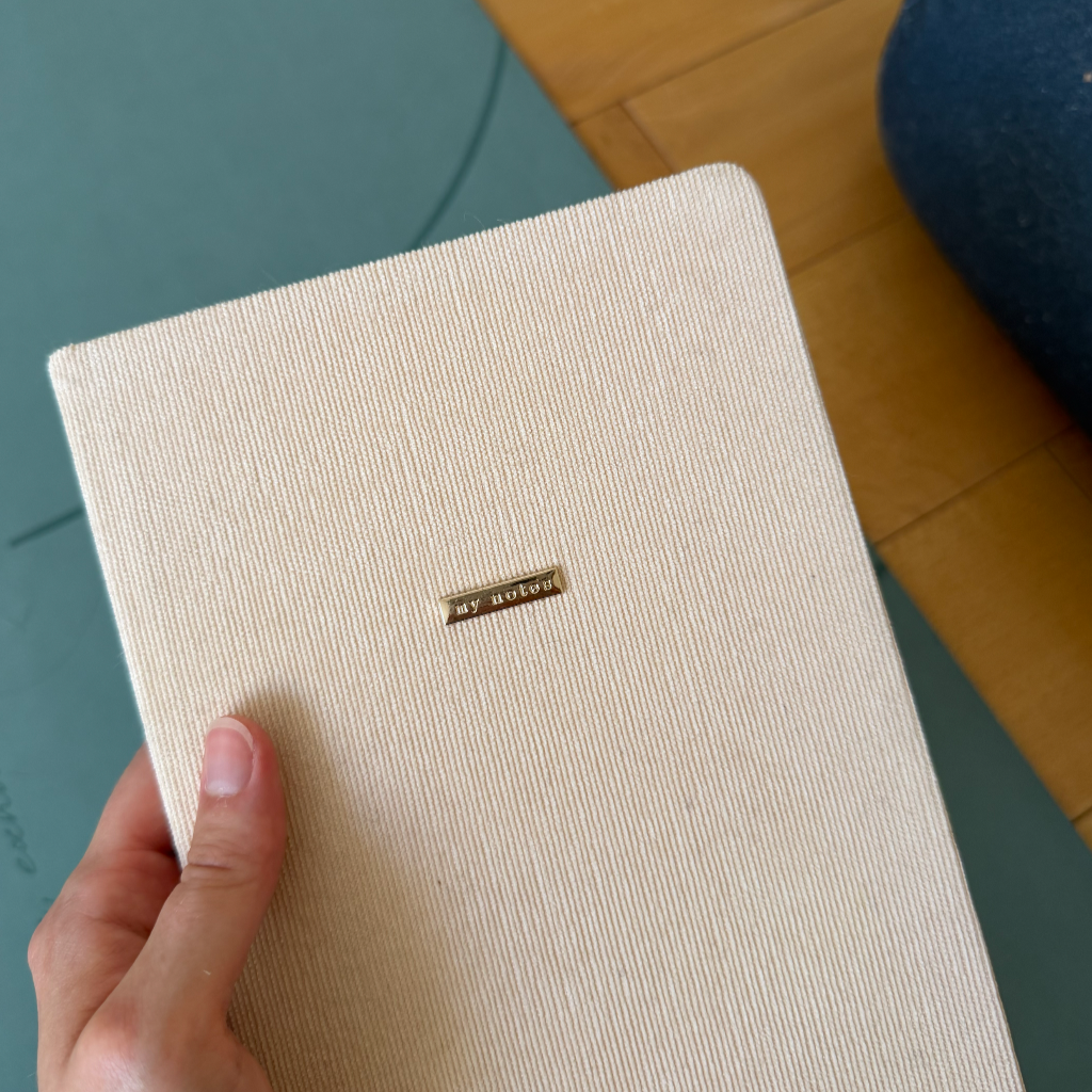 Un carnet fermé dans lequel on peut faire du journaling, photo prise du dessus avec un tapis de yoga et un bolster à côté