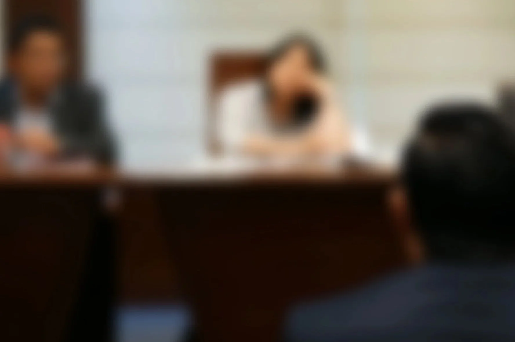 A blurry photo of a person sitting at a desk with a dog sitting on the desk, and another person sitting across from them.