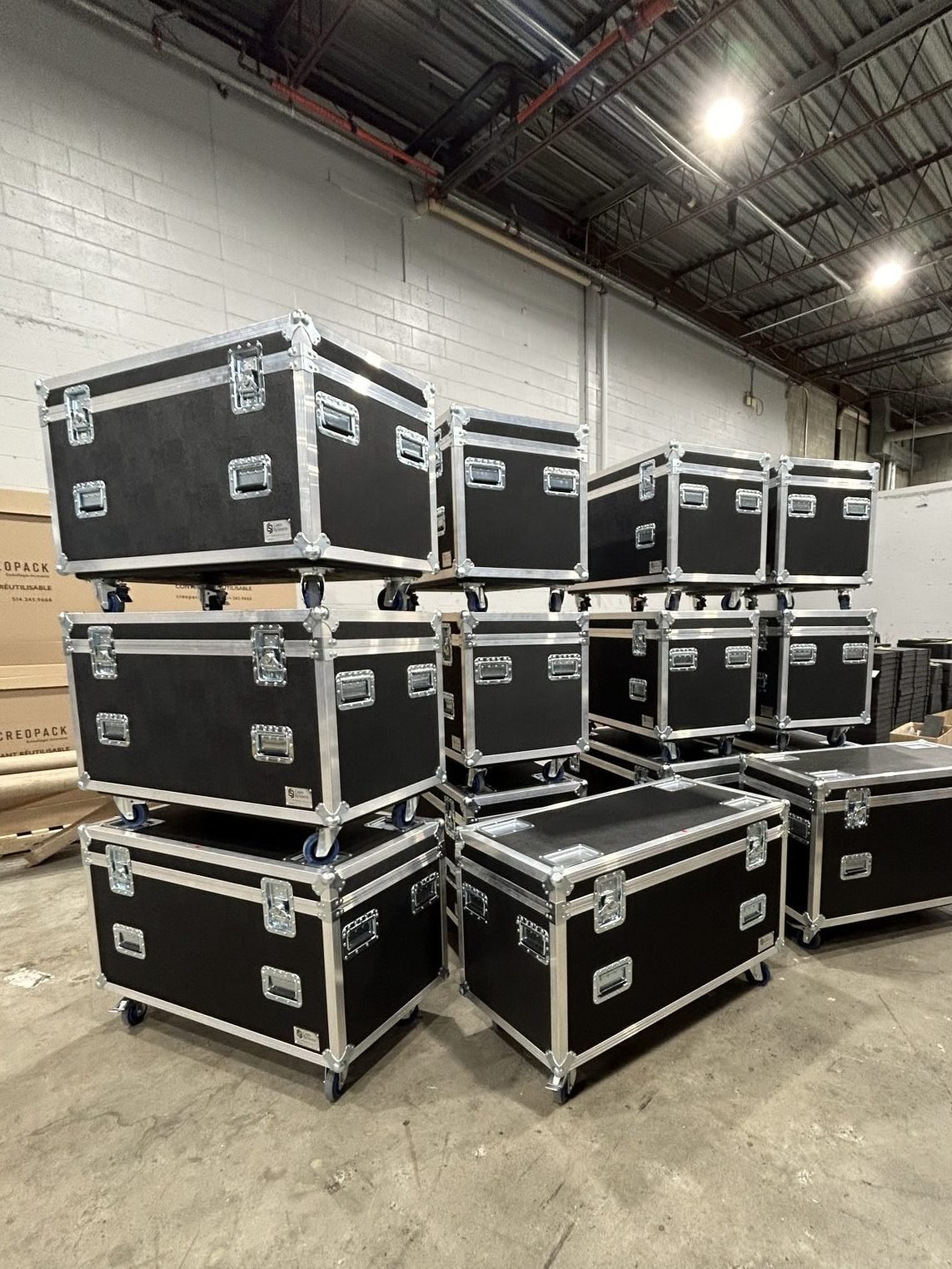 Multiple black flight cases with silver edges and handles stacked in a warehouse setting.