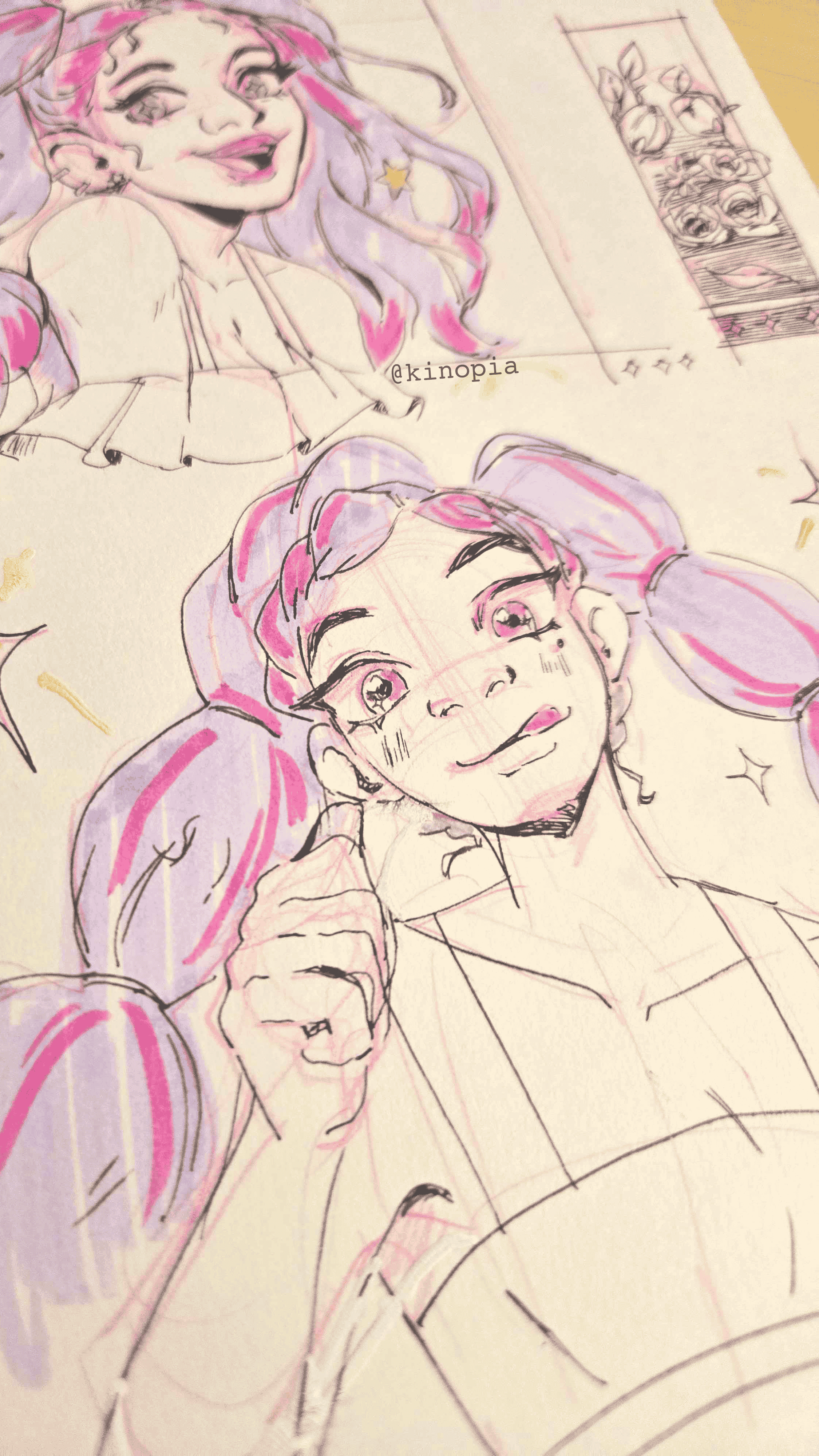 Sketches of two young girls with pink and lavender hair, one with pigtails, smiling and making a playful gesture, drawn on paper with a comic strip and a character reference in the background.