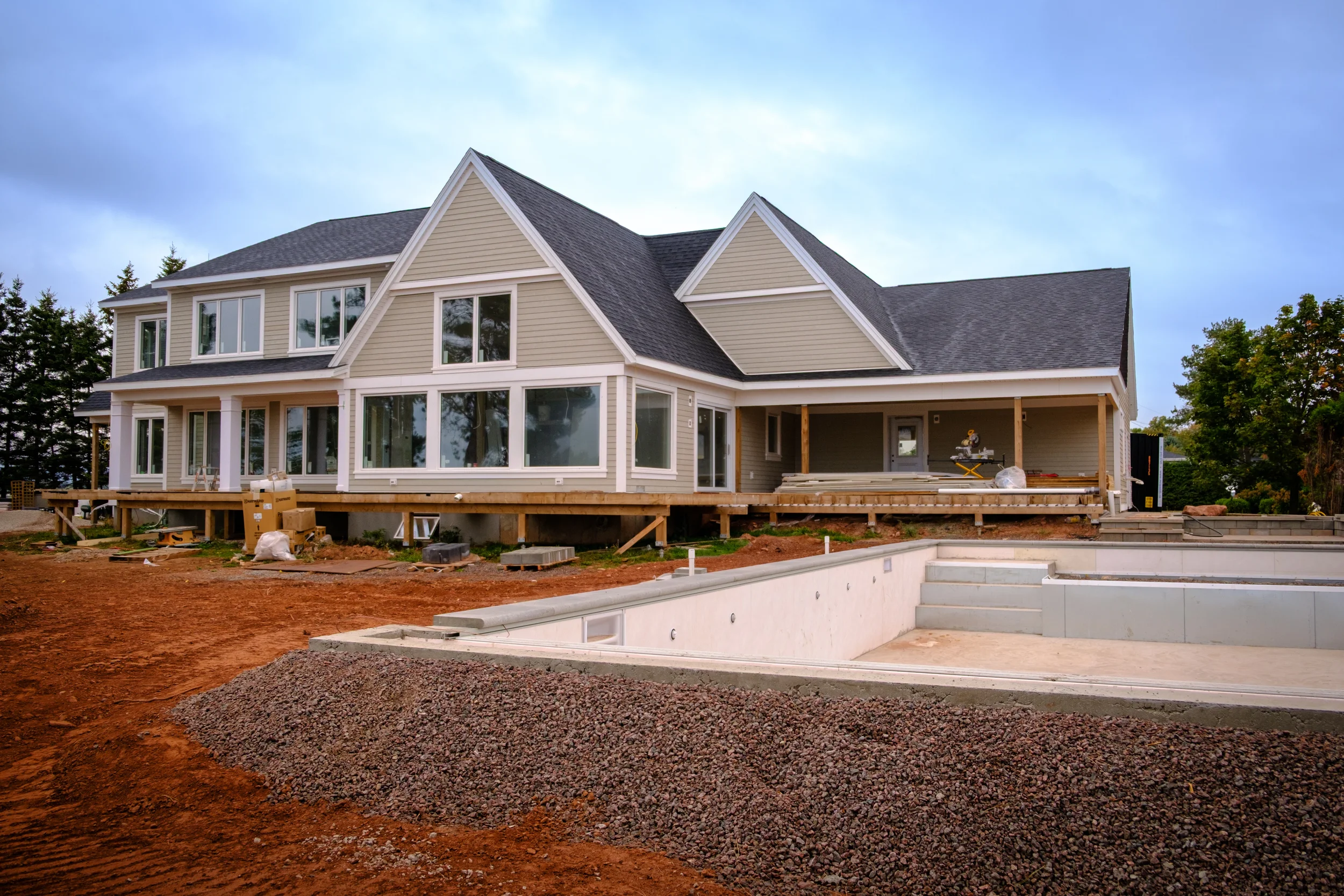 A large house under construction with a backyard pool area still being built, featuring a raised deck and construction materials around.