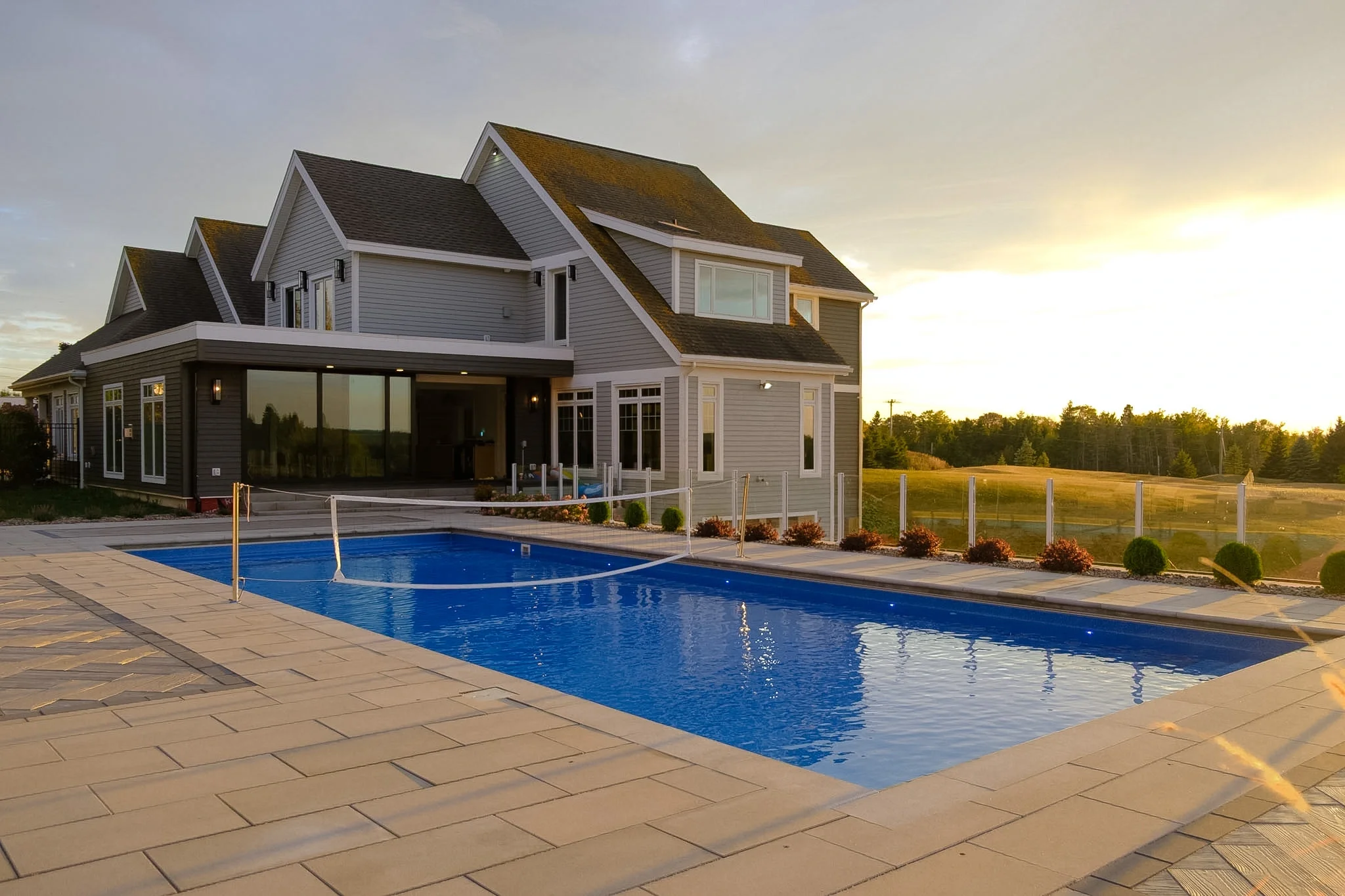 A modern two-story house with gray siding, large windows, and a backyard swimming pool during sunset.