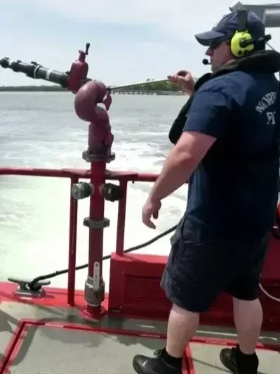 A person standing on a boat overlooking water, with a fire hydrant mounted on the boat's railing, and the hydrant's nozzle pointing outward.