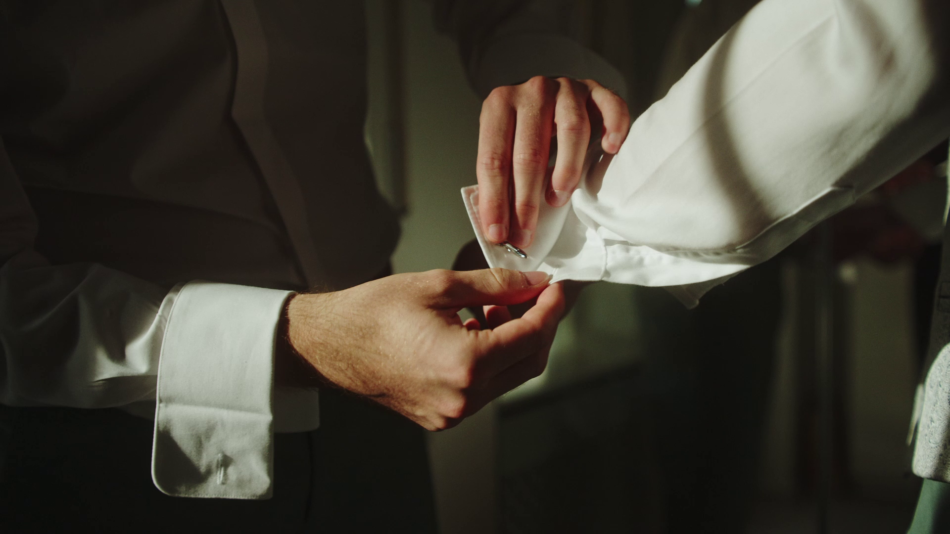 Nahaufnahme eines Bräutigams beim getting ready, der einen weißen Hemdärmel zuknöpft.