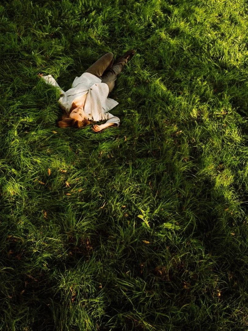 Eine Frau liegt auf einer Wiese, umgeben von grünem Gras, an einem sonnigen Tag. Hochzeitsfotos München, Nürnberg