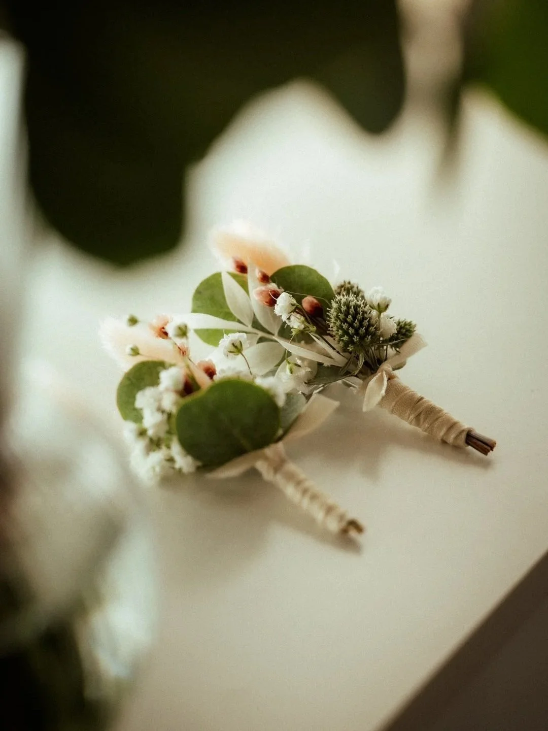 Zwei kleine Blumensträuße mit weißen und grünen Blumen, eingewickelt in helles Tuch, auf einer weißen Oberfläche.