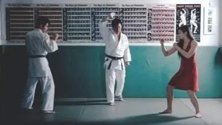 Three people practicing martial arts in a dojo with charts and posters on the wall.