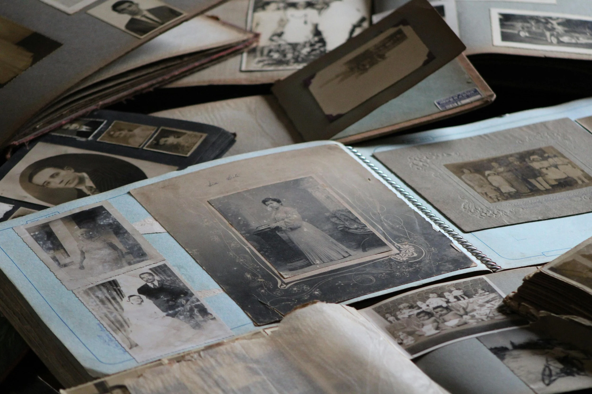 A collection of vintage black-and-white photographs and photo albums open on a table, featuring portraits and group photos, some in decorative frames.