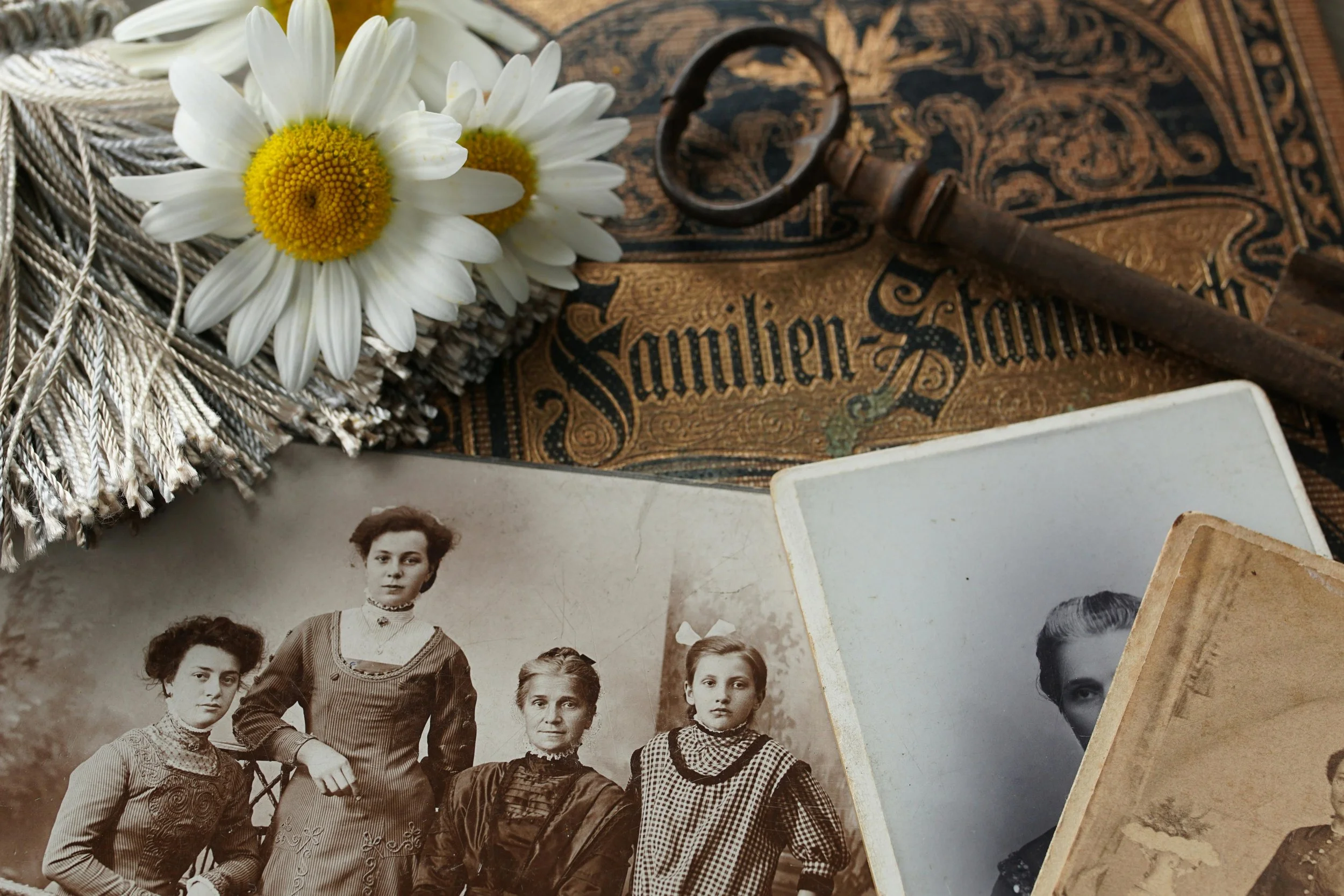 Vintage black and white photographs of women and girls, an antique key, white daisies, and a decorative cloth with the word "Samliem" or similar script.