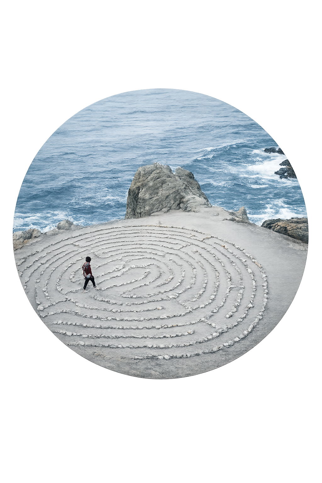 A person walking through a circular spiral sand maze on a rocky beach with ocean waves in the background.