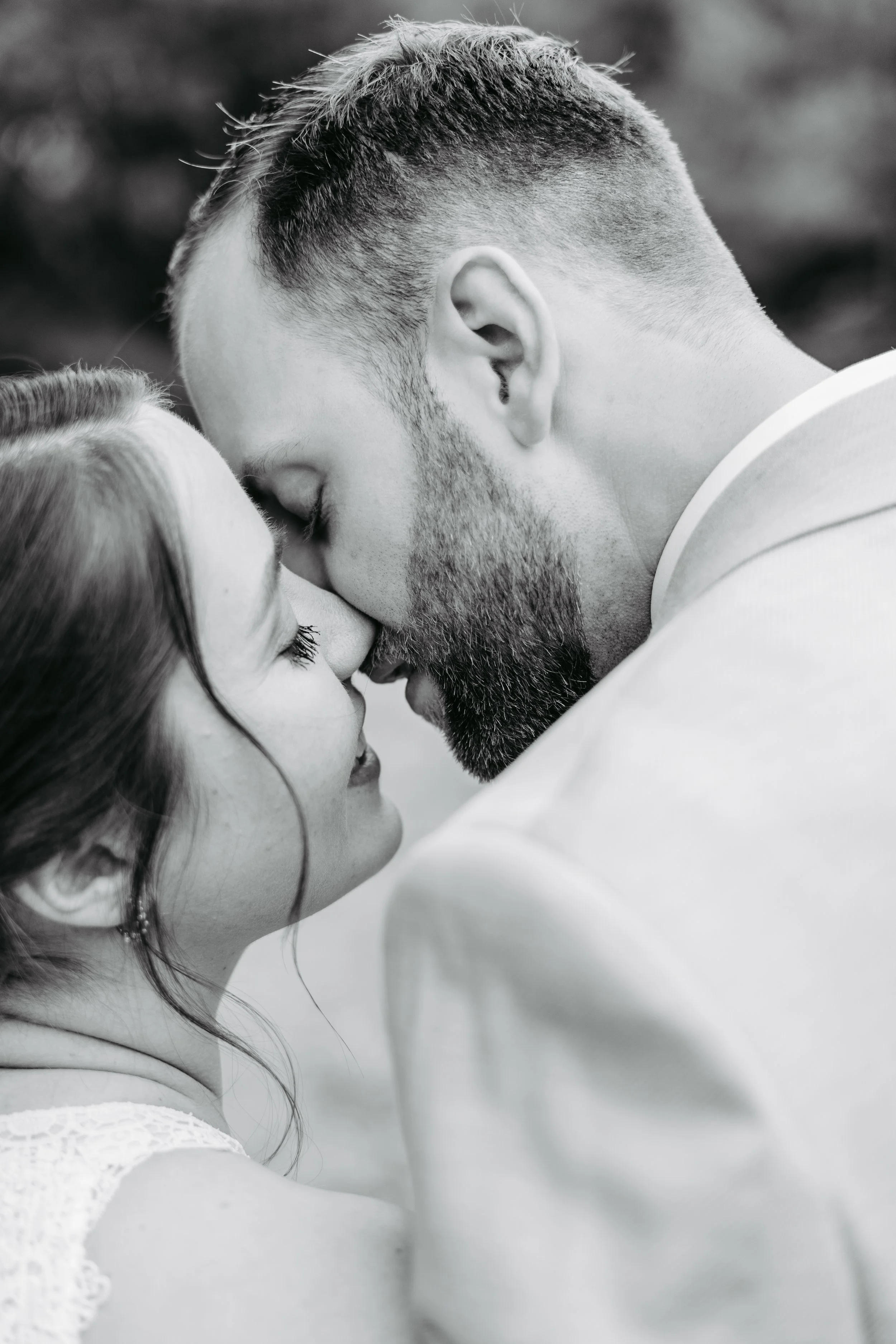 Ein Paar, vermutlich frisch verheiratet, steht sich nah und berührt ihre Nasen, während sie sich liebevoll anschauen, in Schwarz-Weiß.