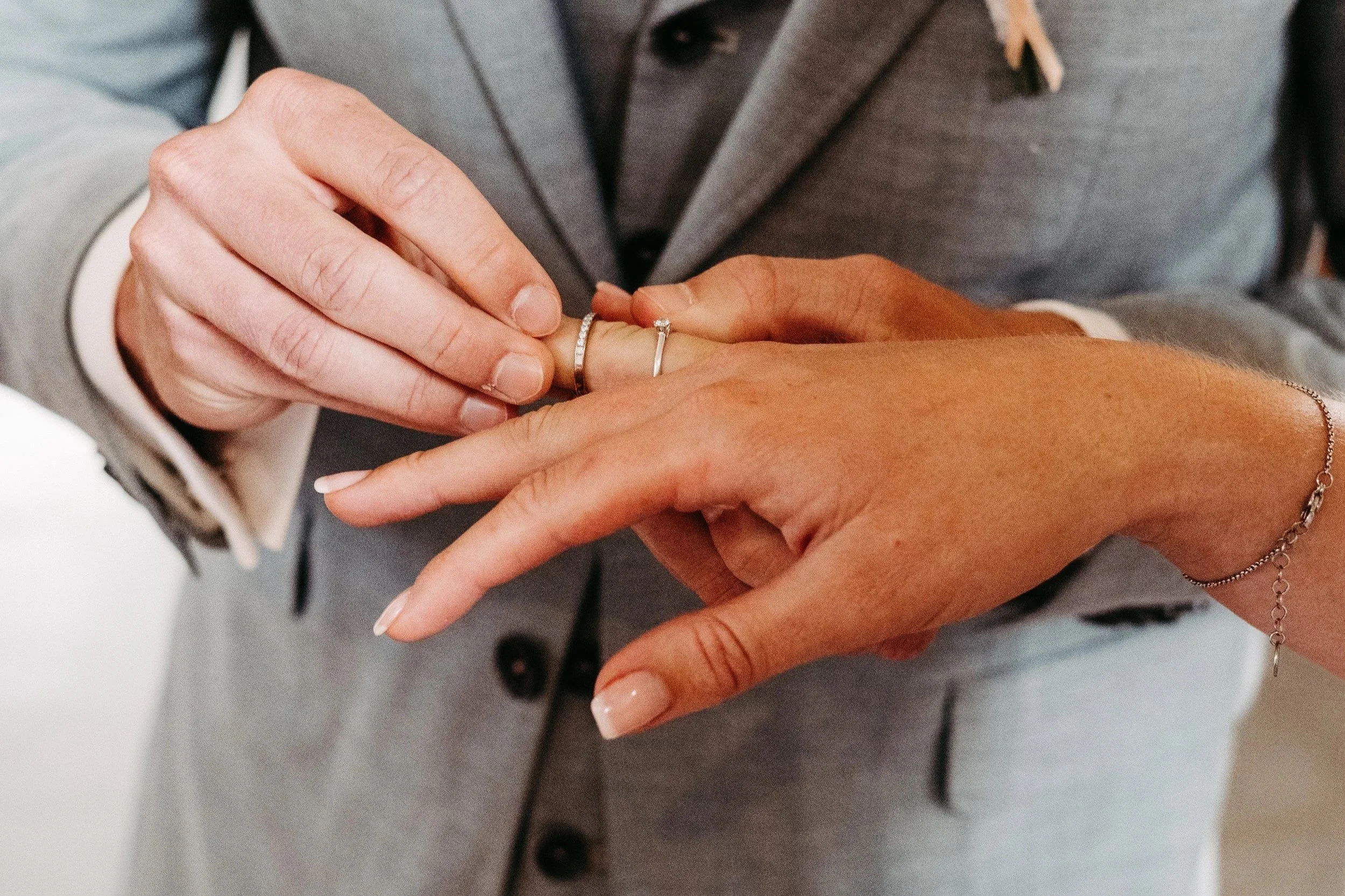 Ein Mann in einem grauen Anzug steckt einer Frau einen Heiratsring an den Finger.