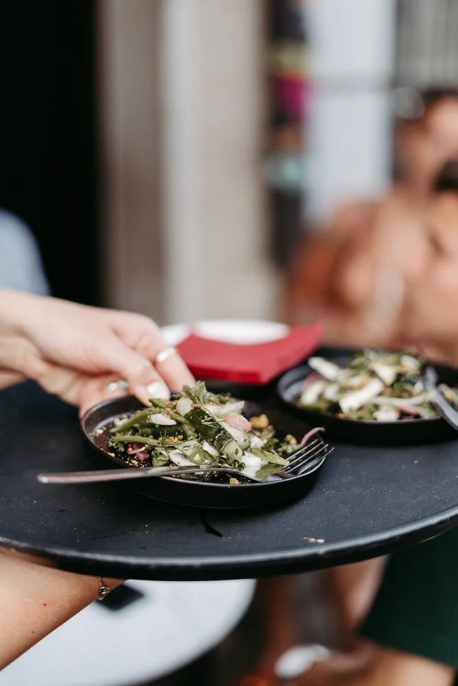 Person serviert Salat auf schwarzen Tellern.