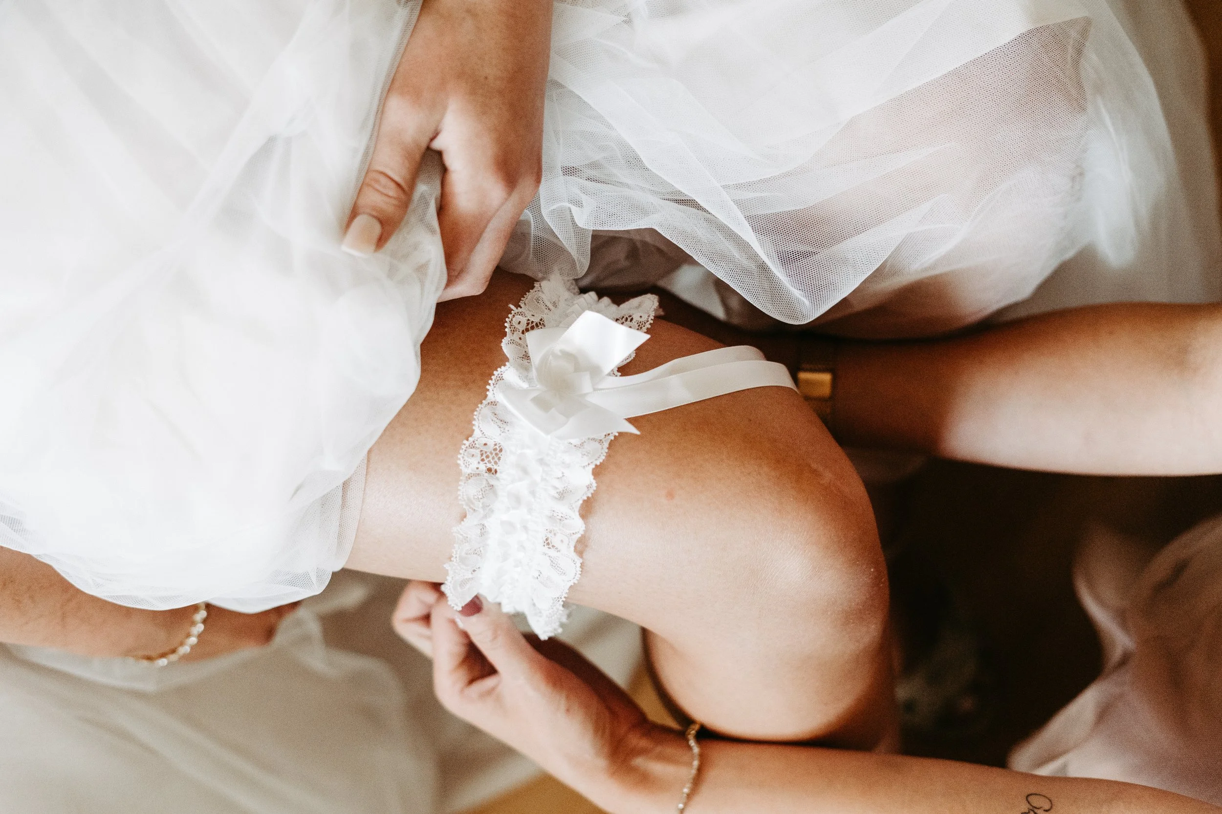 Nahaufnahme einer Person, die einen weißen Spitzen-Garter mit Schleife an ihrem Bein während der Hochzeitsvorbereitungen trägt.