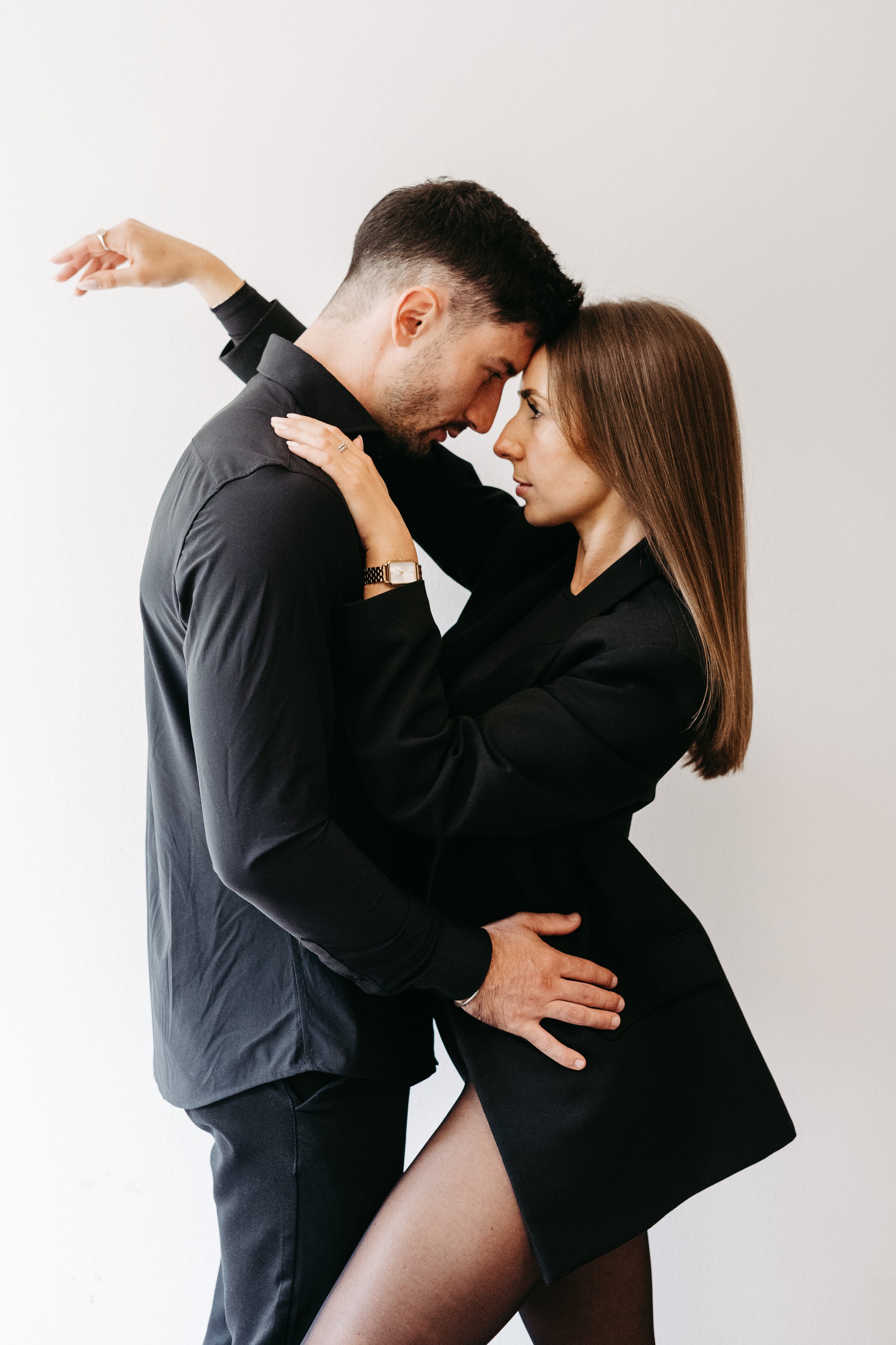 Ein Mann und eine Frau stehen eng umschlungen vor einem weißen Hintergrund, sie blicken sich intensiv an.