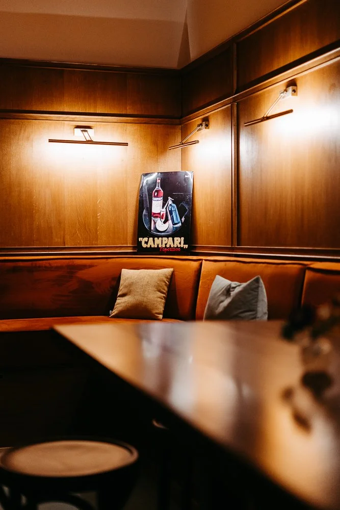 Ein gemütliches Restaurant mit Holzverkleidungen, einer Sitzbank mit Kissen, und einem Wandbild eines Champagner-Getränks im Vintage-Stil.