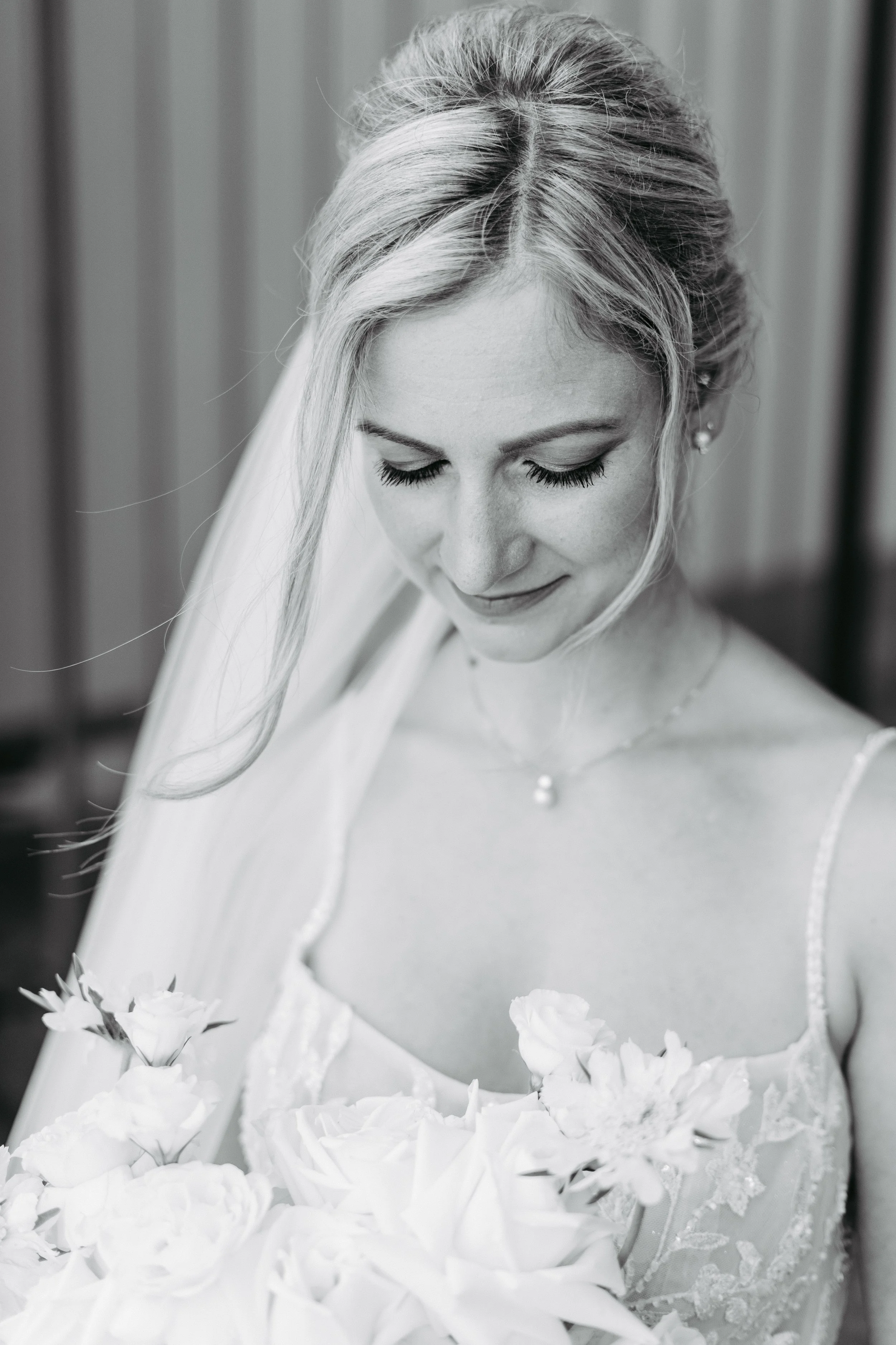 Schwarz-weiß-Foto einer Braut, die nach unten schaut, mit Hochzeitskleid und Blumen in den Armen.